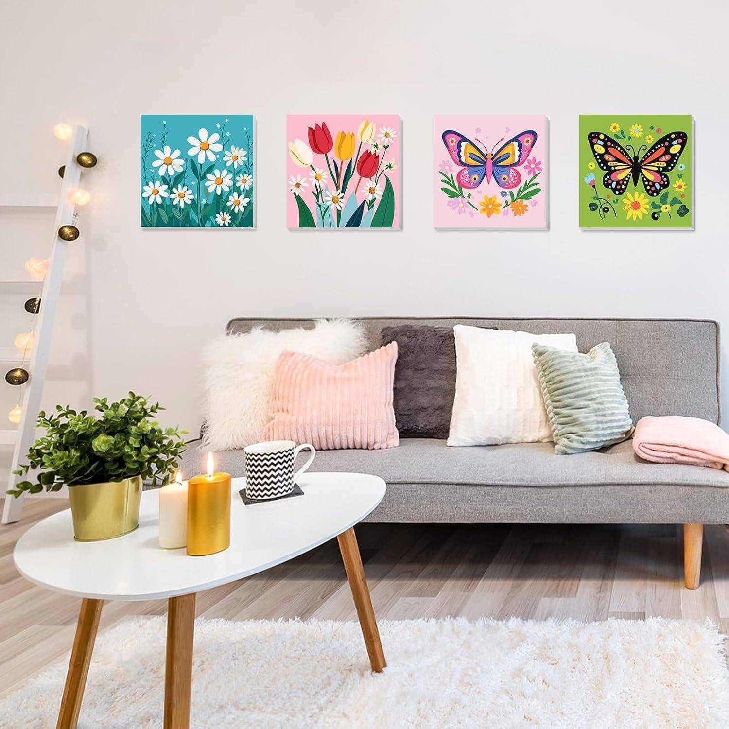 Helles Wohnzimmer mit grauem Sofa, weißem Couchtisch, Pflanzen, Kerzen und vier bunten Schmetterlings- und Blumen-Wanddrucken über dem Sofa.