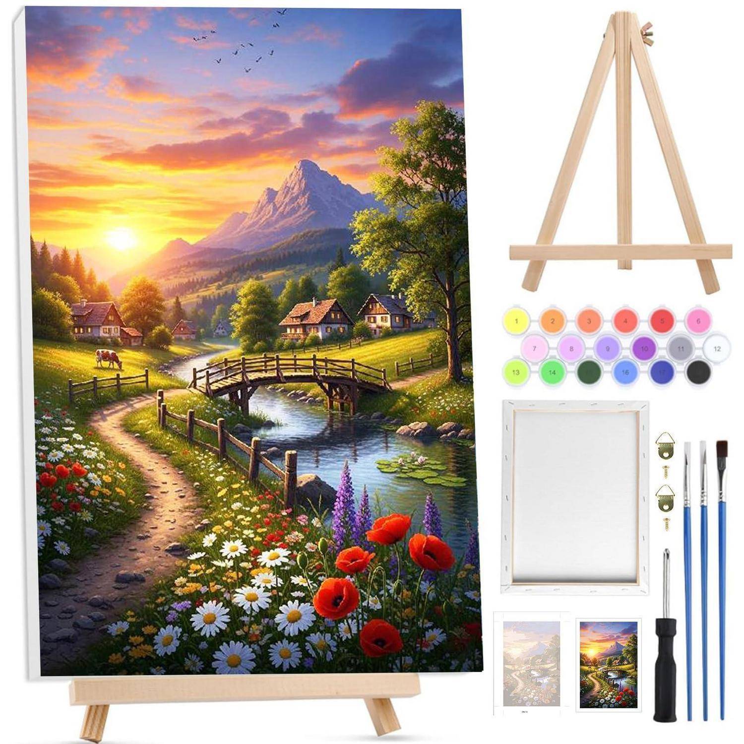 Malkitset mit einer leeren Leinwand auf einer Staffelei, Farben und Pinsel neben einem Referenzbild einer Landschaftsszene mit einem Bergsonnenaufgang über einem Fluss, einer Brücke und Blumen.