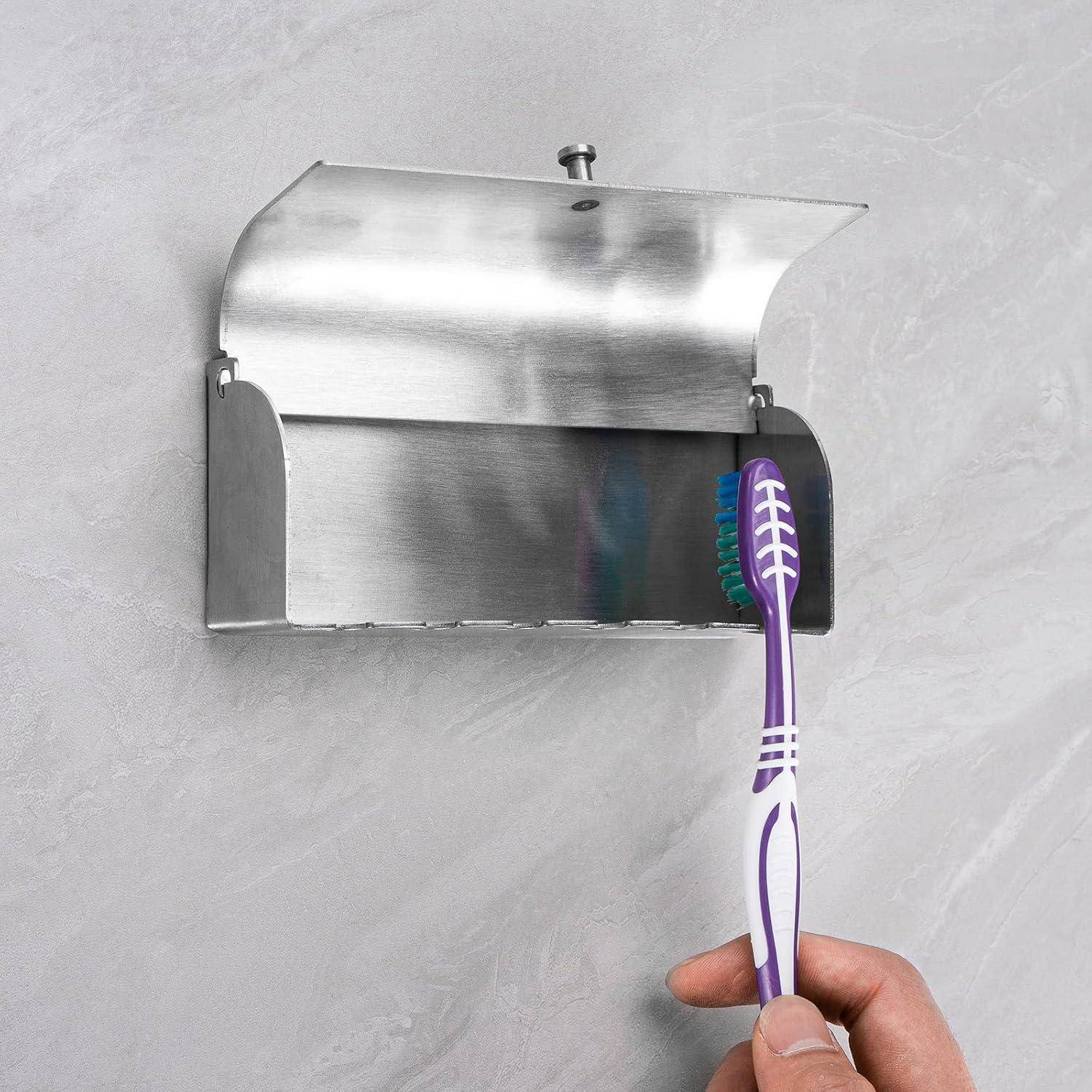 Eine Hand, die eine violette Zahnbürste verwendet, um einen an der Wand montierten Edelstahlhalter oder -spender auf einer gekachelten Wand zu reinigen.