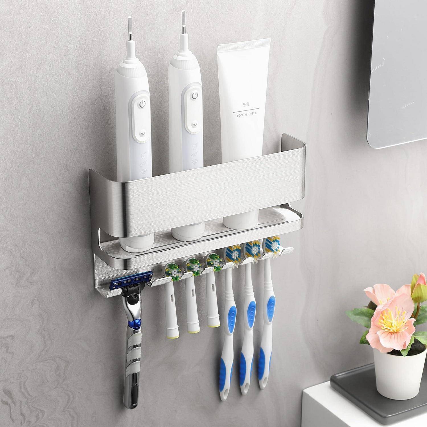 Wandmontierter Badezimmerorganizer, der zwei elektrische Zahnbürsten, eine Zahnpastatube, einen Rasierer und mehrere manuelle Zahnbürsten hält, mit einem kleinen Blumentopf in der Nähe.