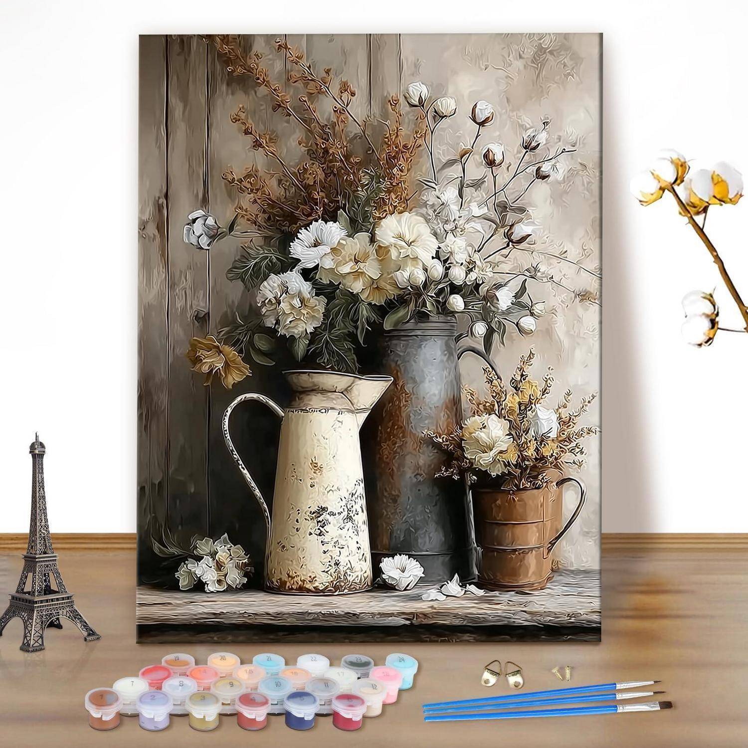 Kunstmaterialien arrangiert vor einem Stillleben-Blumengemälde auf einer Staffelei, mit Farbtöpfen, Pinseln und einer kleinen Eiffelturm-Figur auf einem Holztisch.