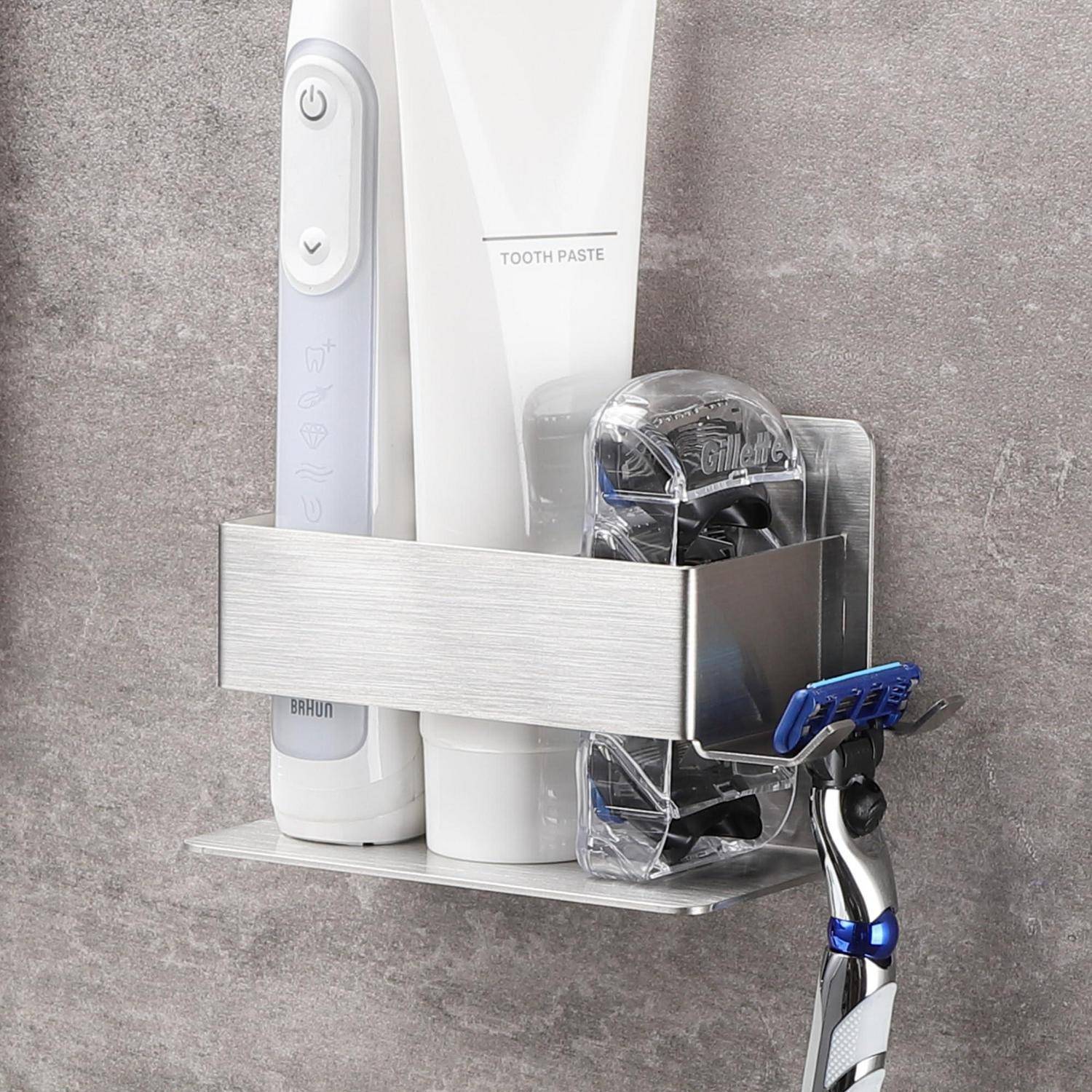 Wandmontierter Badezimmerorganizer, der eine elektrische Zahnbürste, eine Zahnpastatube und einen Rasierer gegen eine graue Fliesenwand hält.