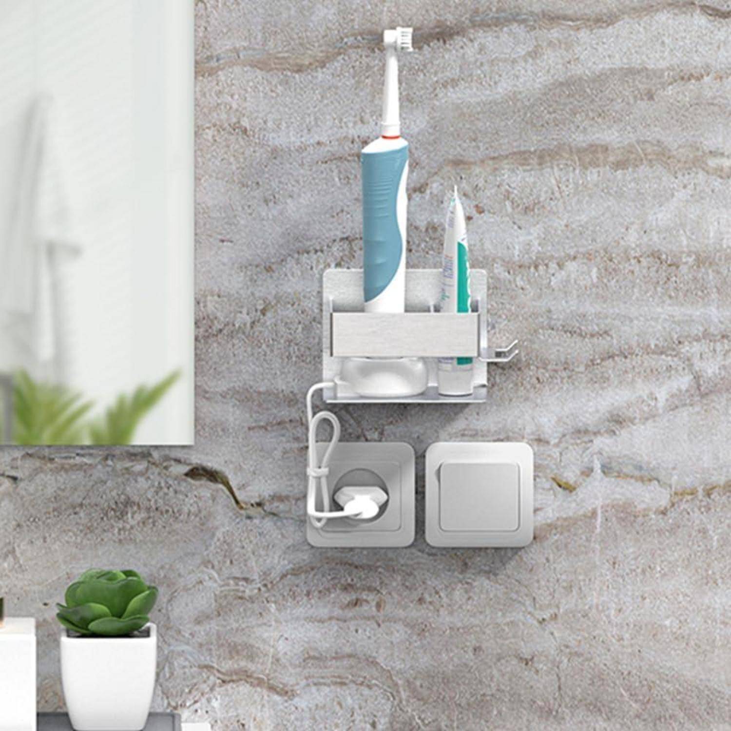 Badezimmer-Wandorganizer, der eine elektrische Zahnbürste und Zahnpasta über zwei wandmontierten Schaltern und einer Steckdose hält, mit einer kleinen Pflanze im Vordergrund.