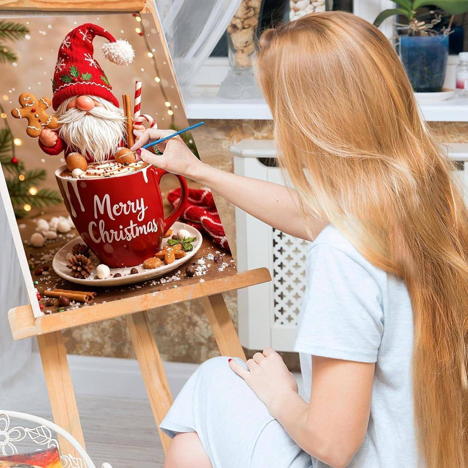 Junge Frau malt ein Weihnachts-Stillleben auf einer Staffelei, das eine rote Tasse mit der Aufschrift 