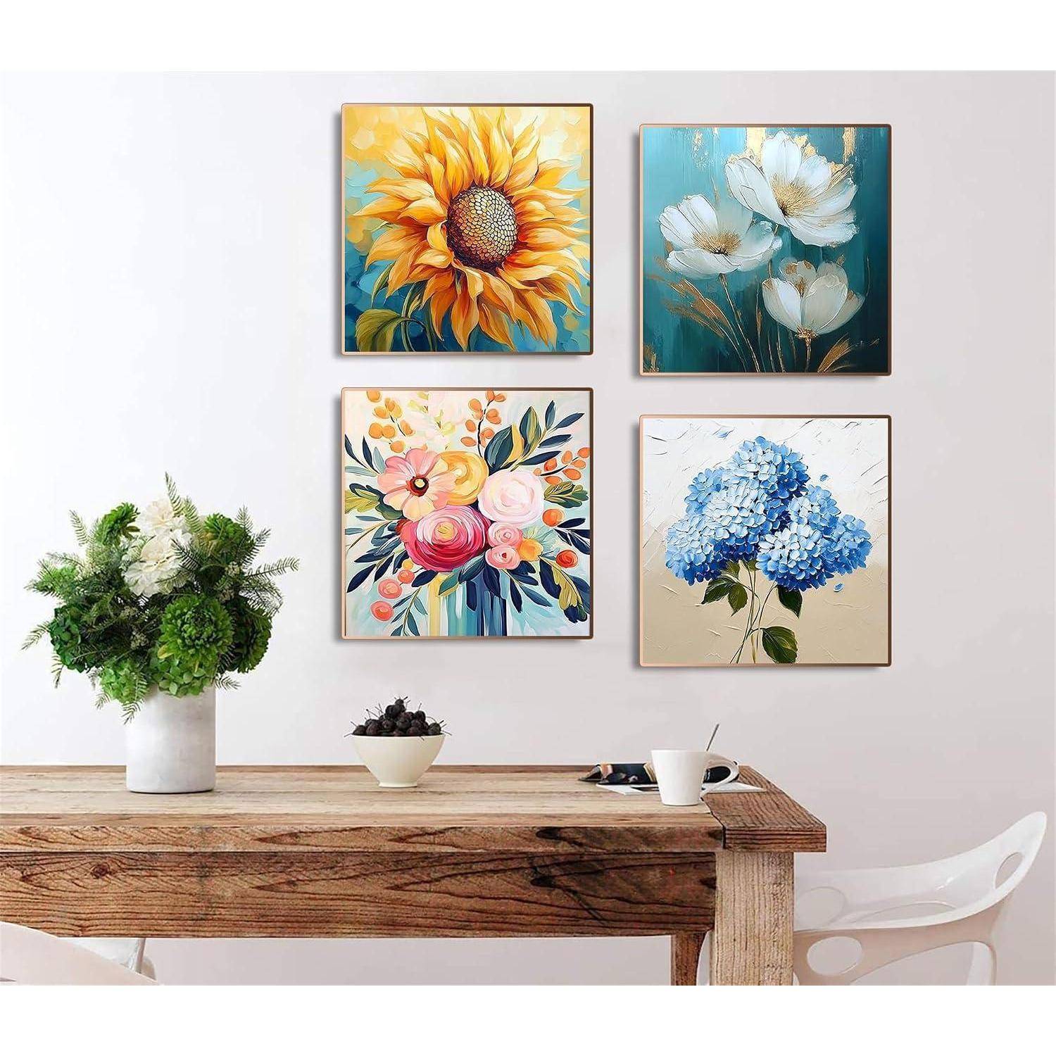 Vier bunte Blumengemälde hängen in einem 2x2-Raster über einem rustikalen Holztisch mit Topfpflanzen und einem weißen Stuhl.