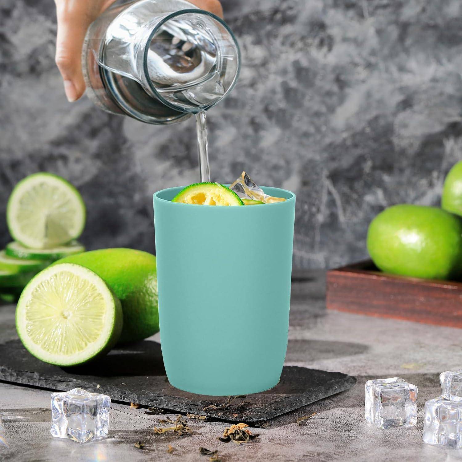 Eine Hand gießt klare Flüssigkeit in eine türkisfarbene Tasse mit Limettenscheiben und Eis, mit ganzen und geschnittenen Limetten auf einer Arbeitsfläche.