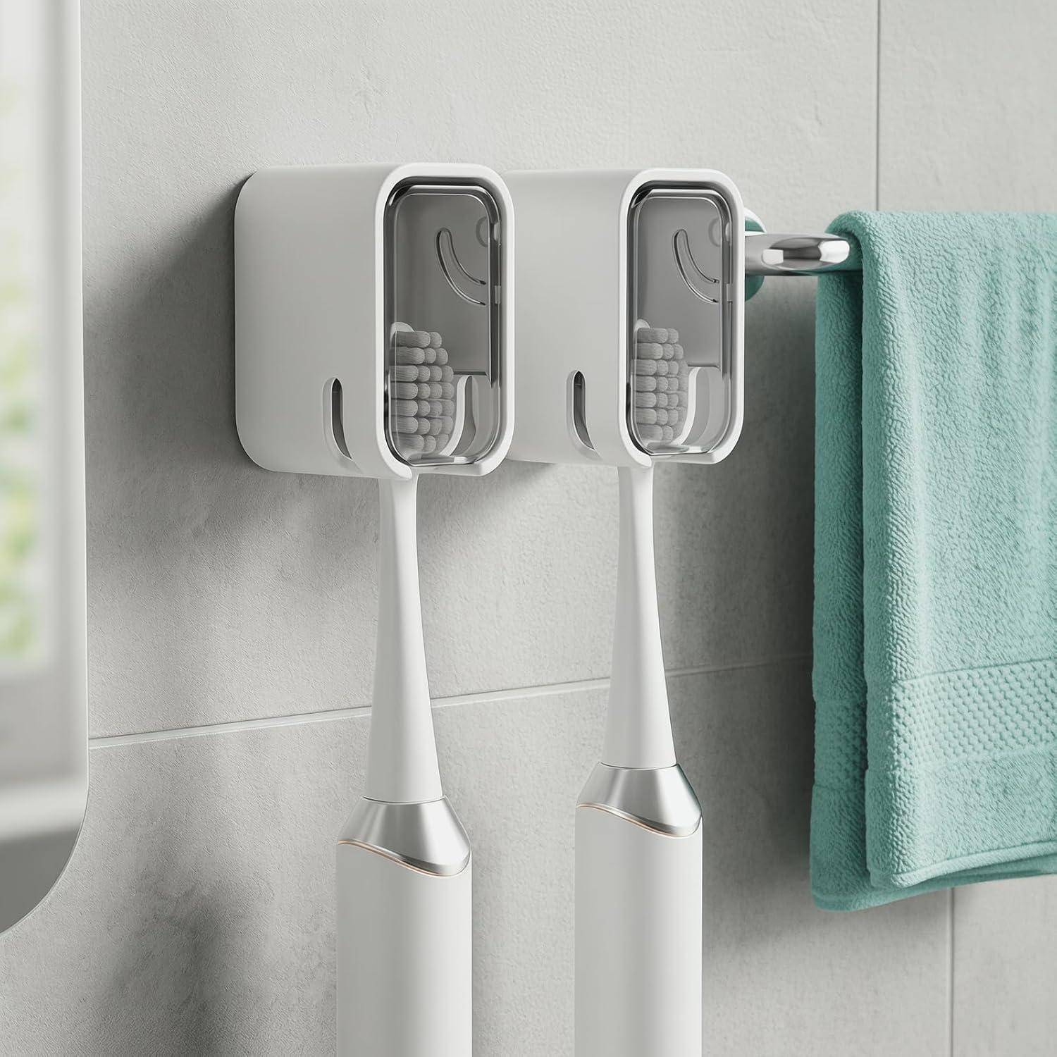 Wandmontierter dualer Elektrozahnbürstenhalter mit Abdeckungen, der zwei Zahnbürsten neben einem hängenden Minztuch im Badezimmer hält.