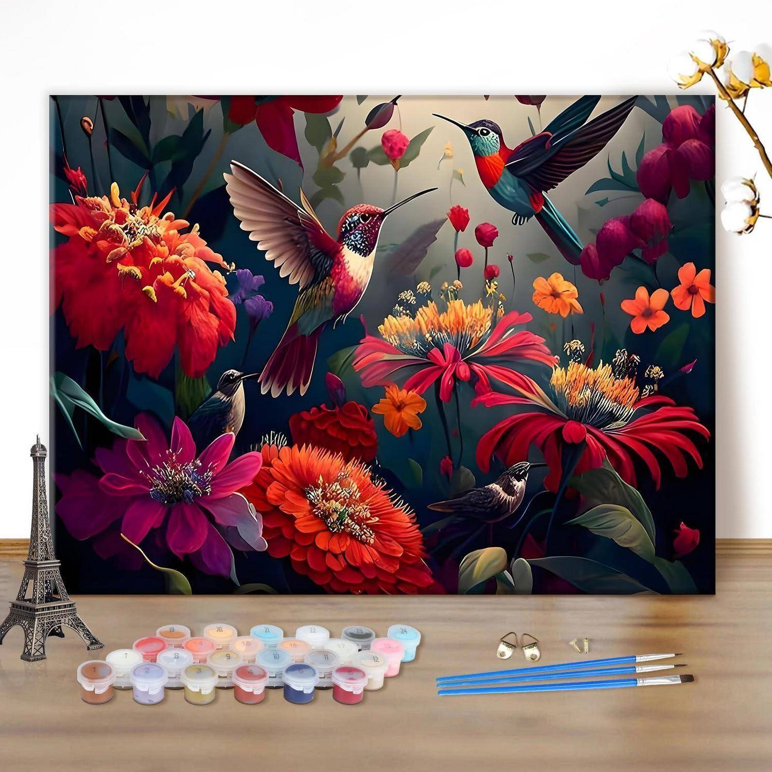 Leinwandgemälde mit farbenfrohen Kolibris und Blumen, mit Farbdosen und Pinseln auf einem Tisch in einer Kunststudio-Umgebung.