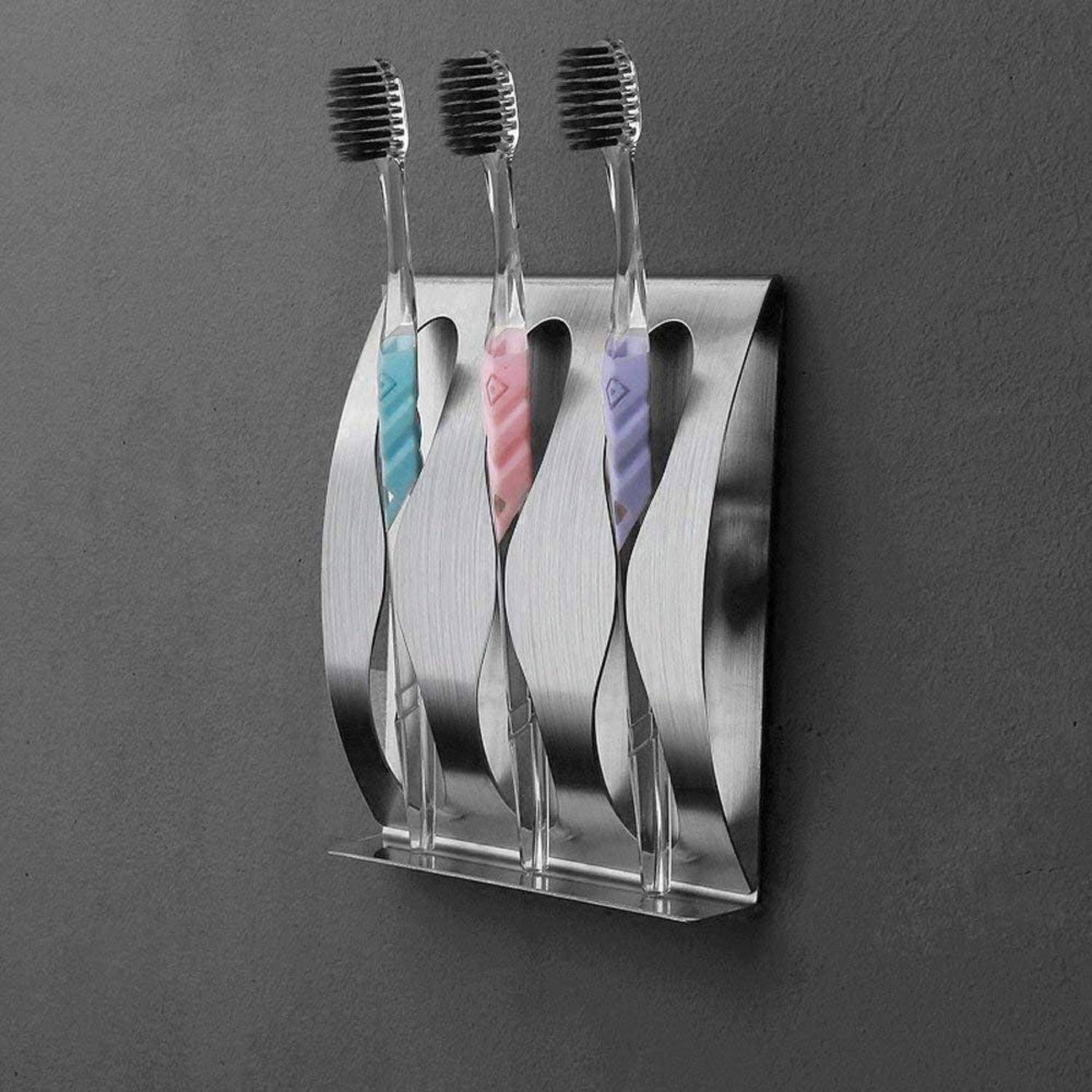 Drei Zahnbürsten in einem an der Wand montierten Edelstahlhalter an einer dunkelgrauen Wand.