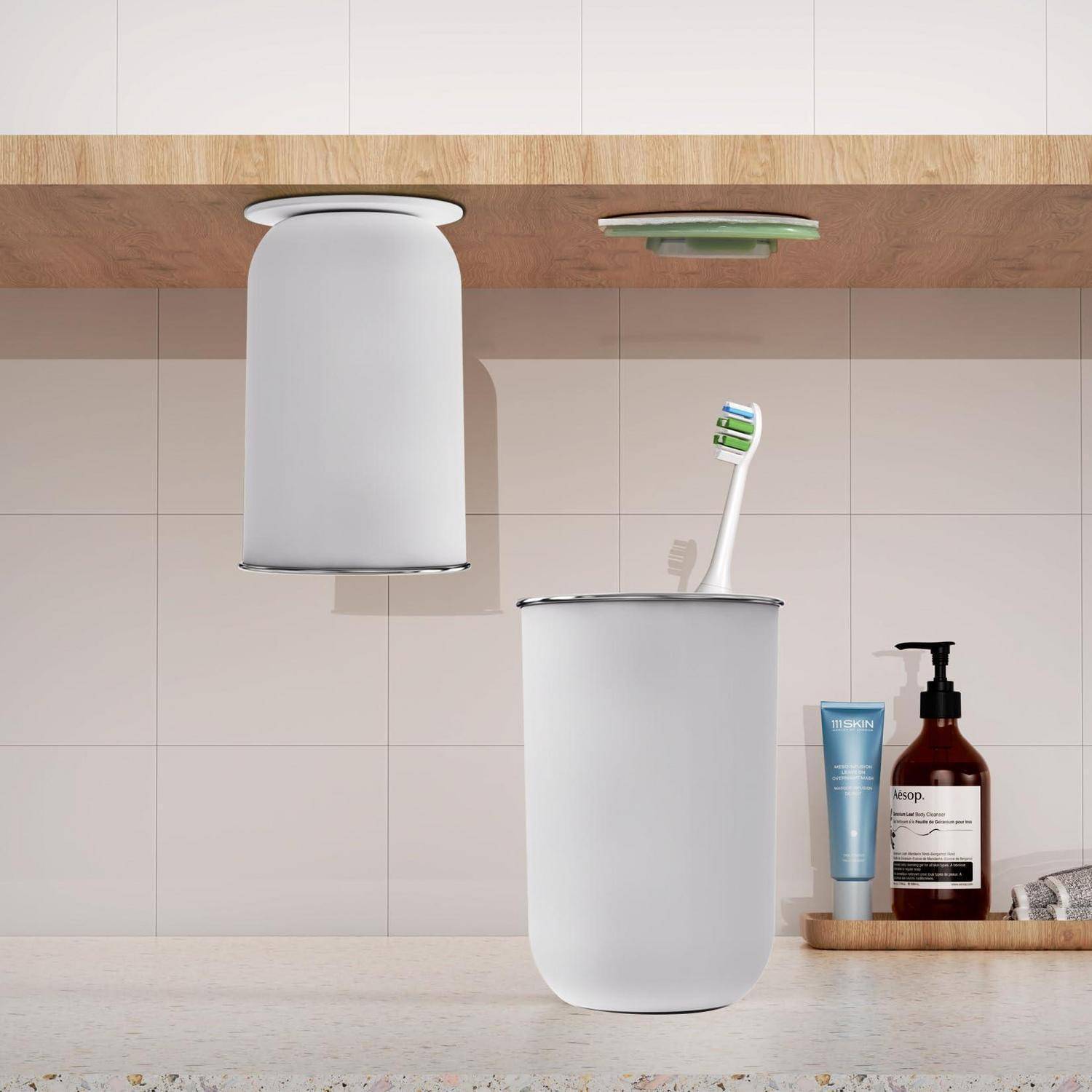 Moderne Badezimmer-Spülaccessoires: ein weißer Zahnbürstenhalter mit Zahnbürste, ein passendes an der Wand montierter Mülleimer und Seifenspender auf einem Waschtisch.