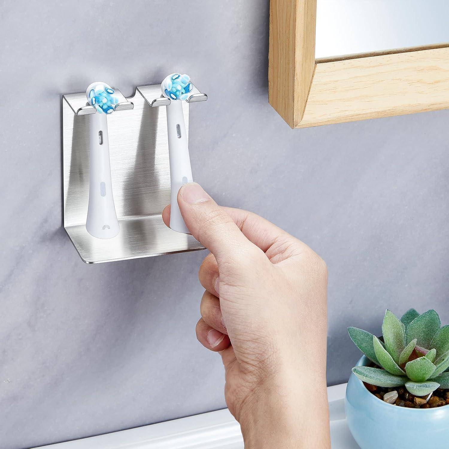 Hand, die eine Zahnbürste in einen an der Wand montierten Edelstahlhalter legt, mit zwei Zahnbürsten neben einem Spiegel und einer kleinen Sukkulente.