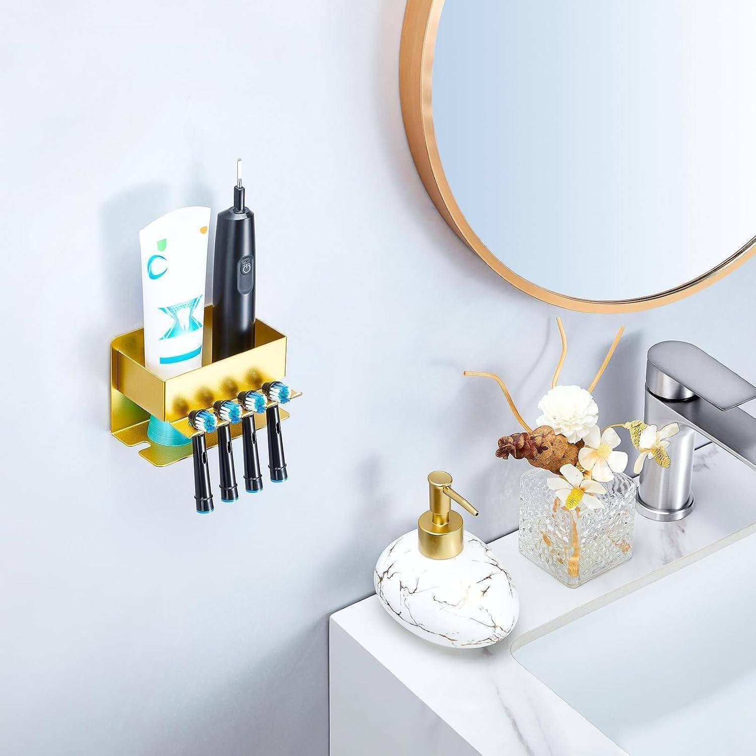 An der Wand montierter goldener Zahnbürstenhalter mit elektrischer Zahnbürste, Zahnpasta und Zubehör neben einem Badezimmerbecken mit Seifenspender, Vase und rundem Spiegel.