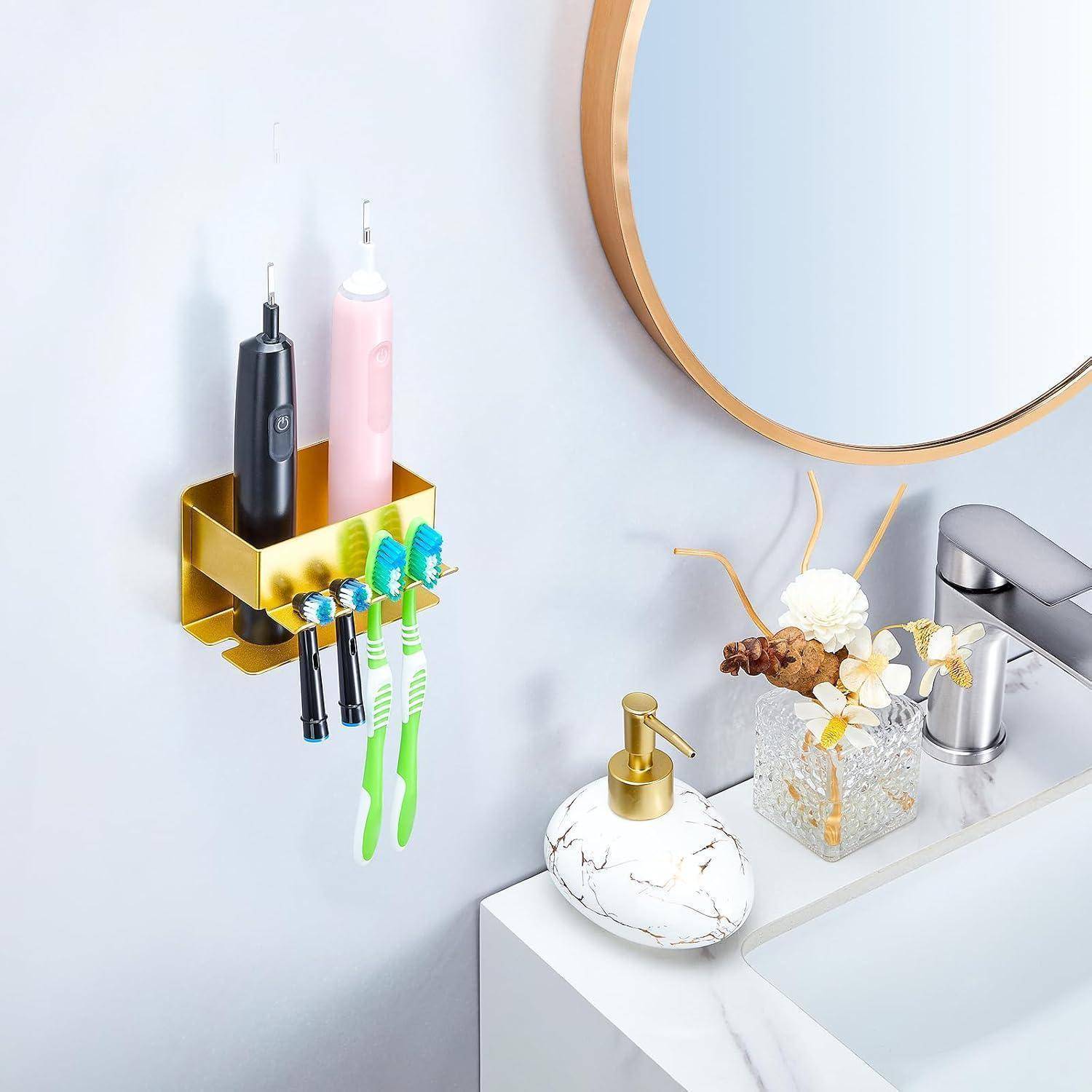 Goldener an der Wand montierter Badezimmerorganizer mit elektrischen Zahnbürsten und zwei Griffen neben einem Waschbecken und rundem Spiegel mit Seifenspender und Blumendekoration.