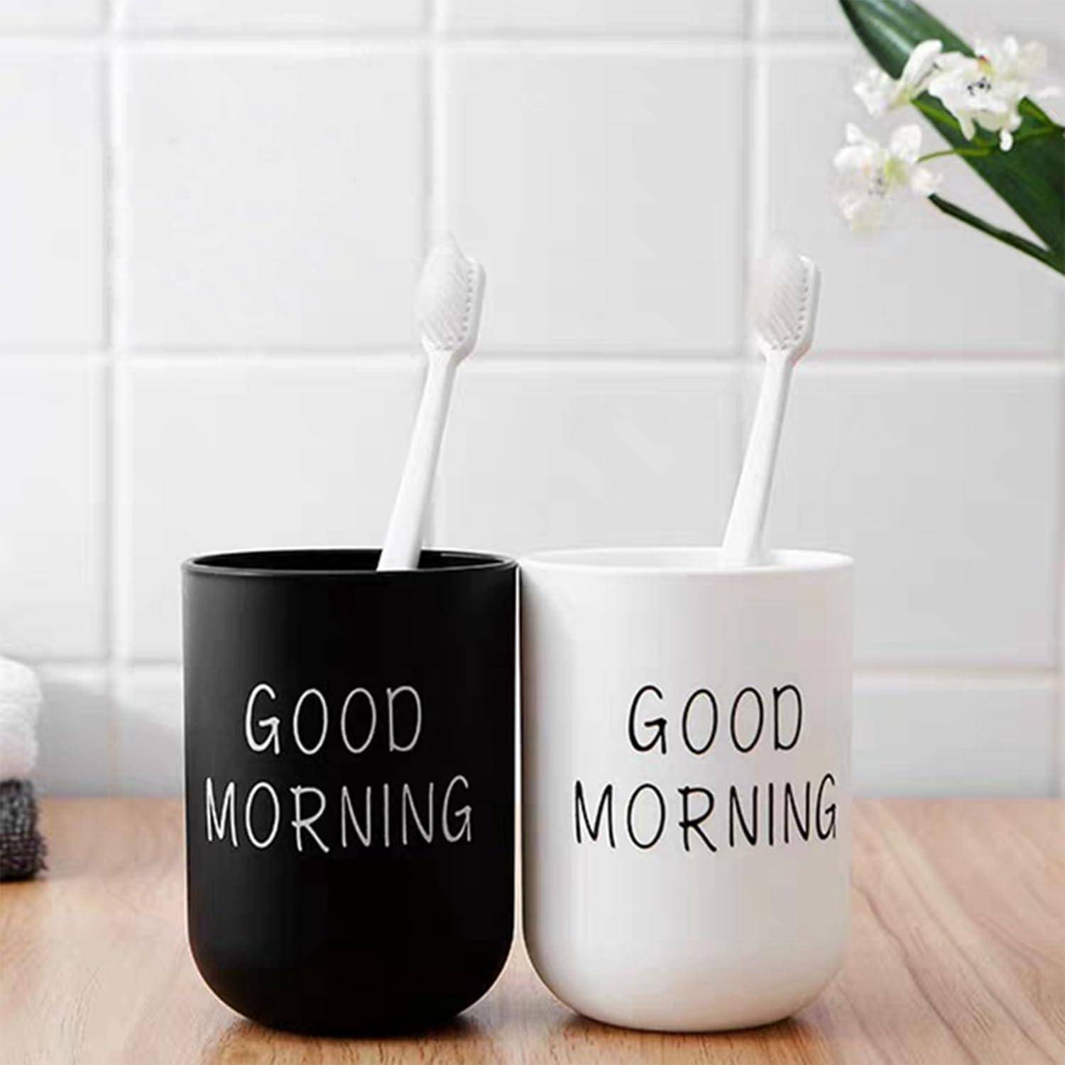 Zwei Zahnbürsten in schwarzen und weißen Bechern mit der Aufschrift „GOOD MORNING