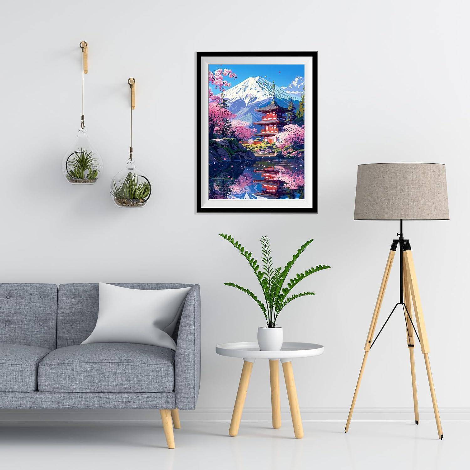 Modernes Wohnzimmer mit grauem Sofa, gerahmtem Kunstwerk mit Berg- und Tempelmotiven, Topfpflanze auf kleinem Tisch, hängenden Blumenkübeln und Stativ-Stehleuchte.