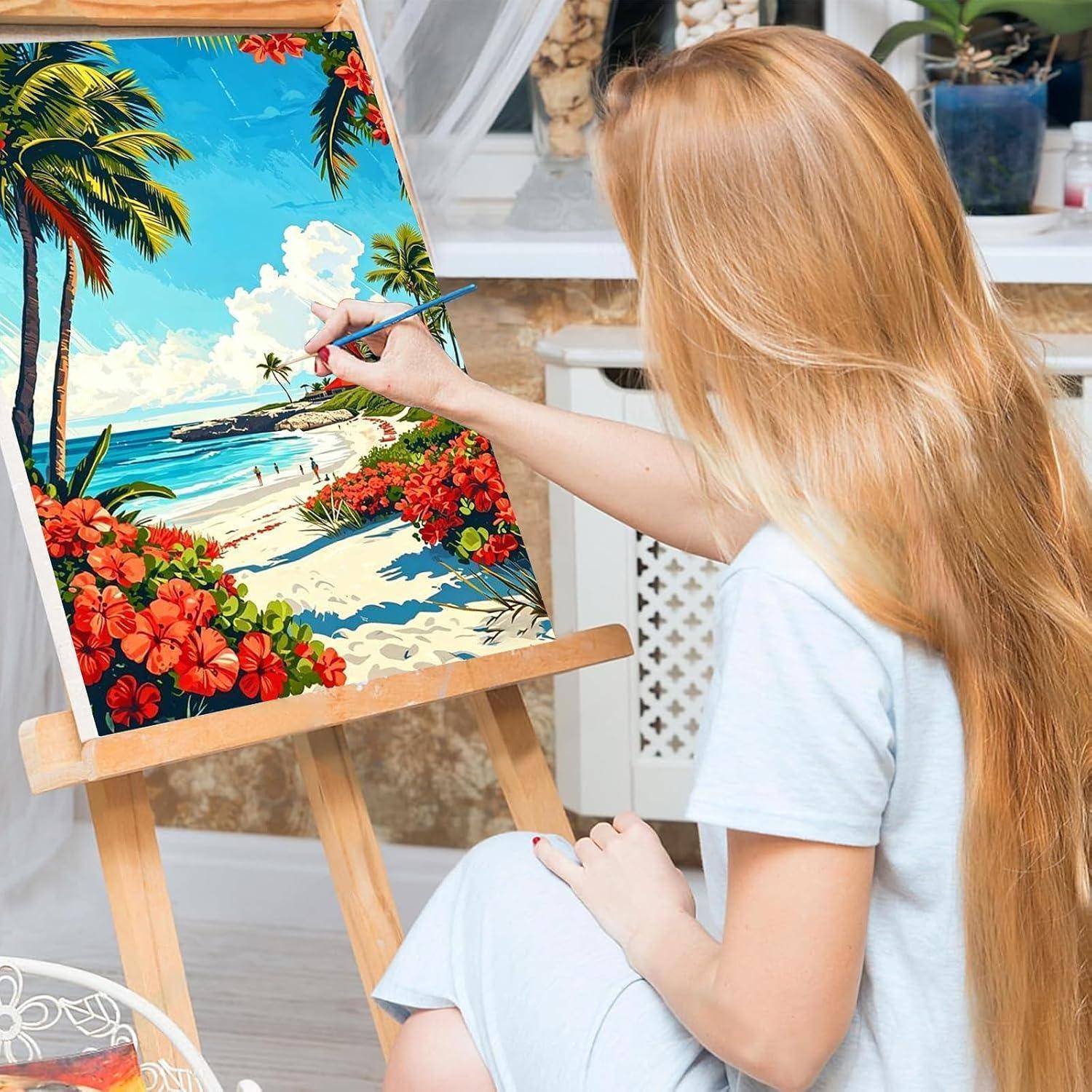 Eine Frau malt eine tropische Strandszene auf einer Staffelei und fügt Details zu einer farbenfrohen Landschaft mit Palmen, Blumen, Sand und Ozean hinzu.