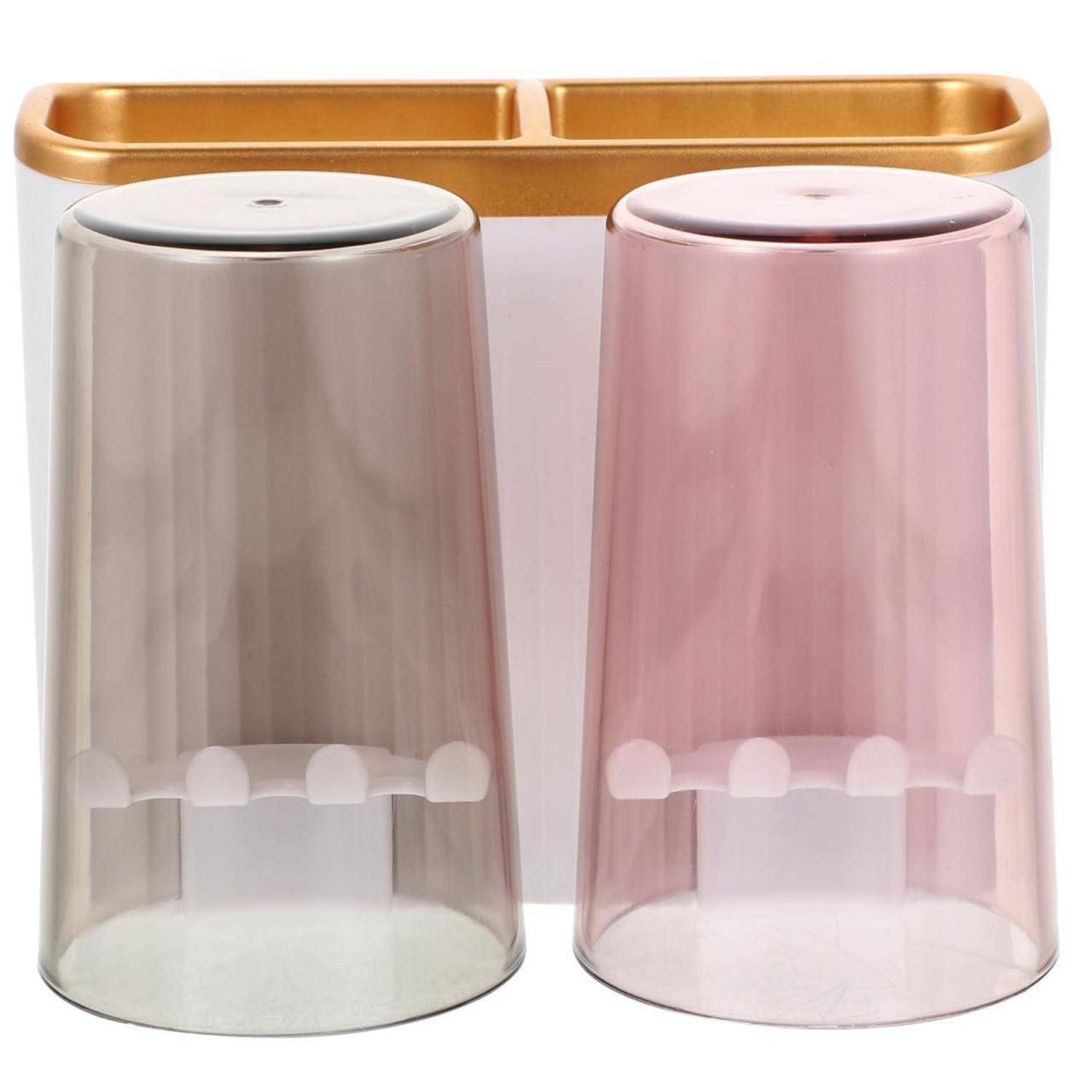 Zwei durchscheinende Trinkgläser, eines in Rauchtönung und eines in Rosa, nebeneinander angeordnet mit goldfarbenem Rand oder Haltern dahinter.
