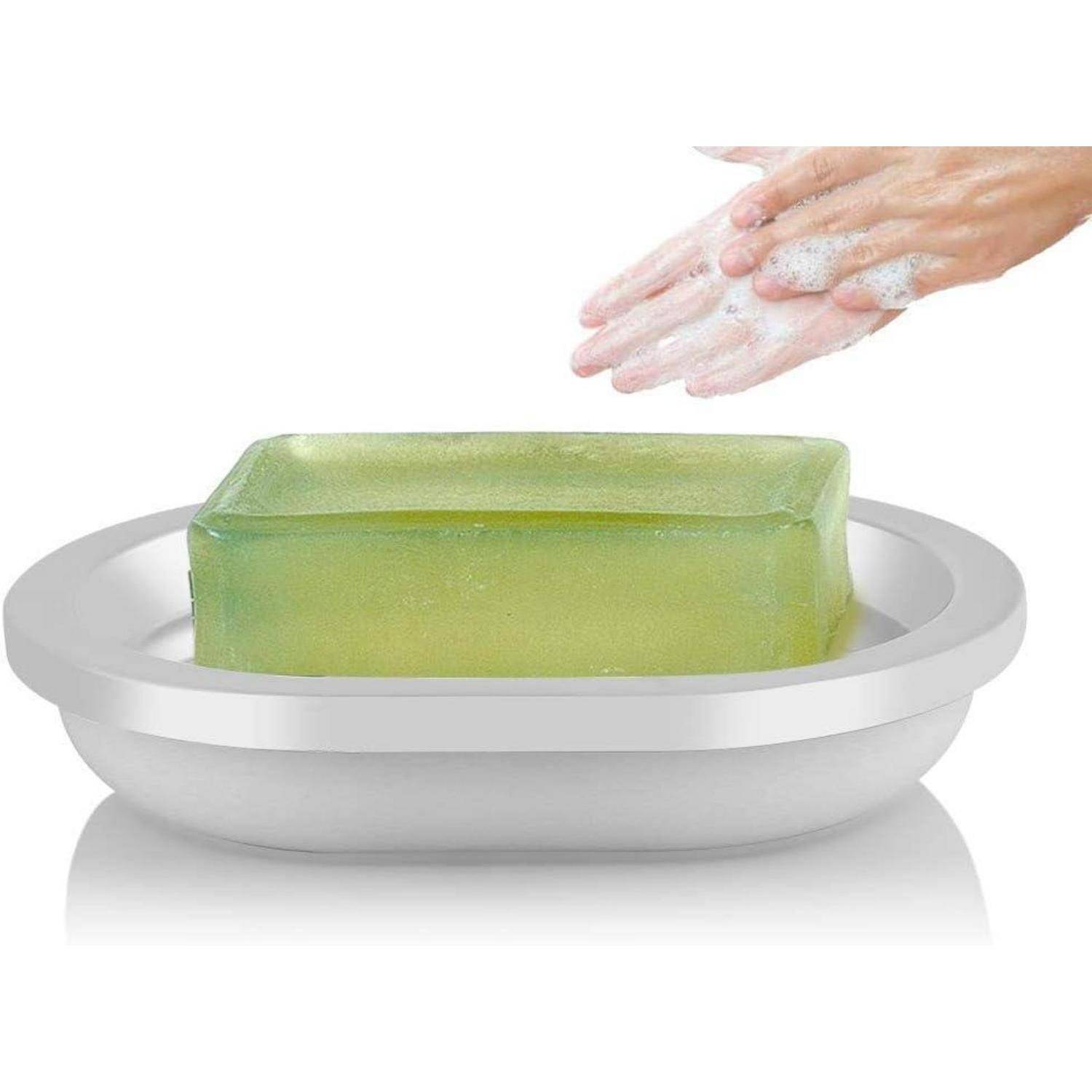 Hände mit Seifenschaum über einem grünen Seifenstück in einer silbernen Schale, das Händewaschen oder Reinigung zeigt.