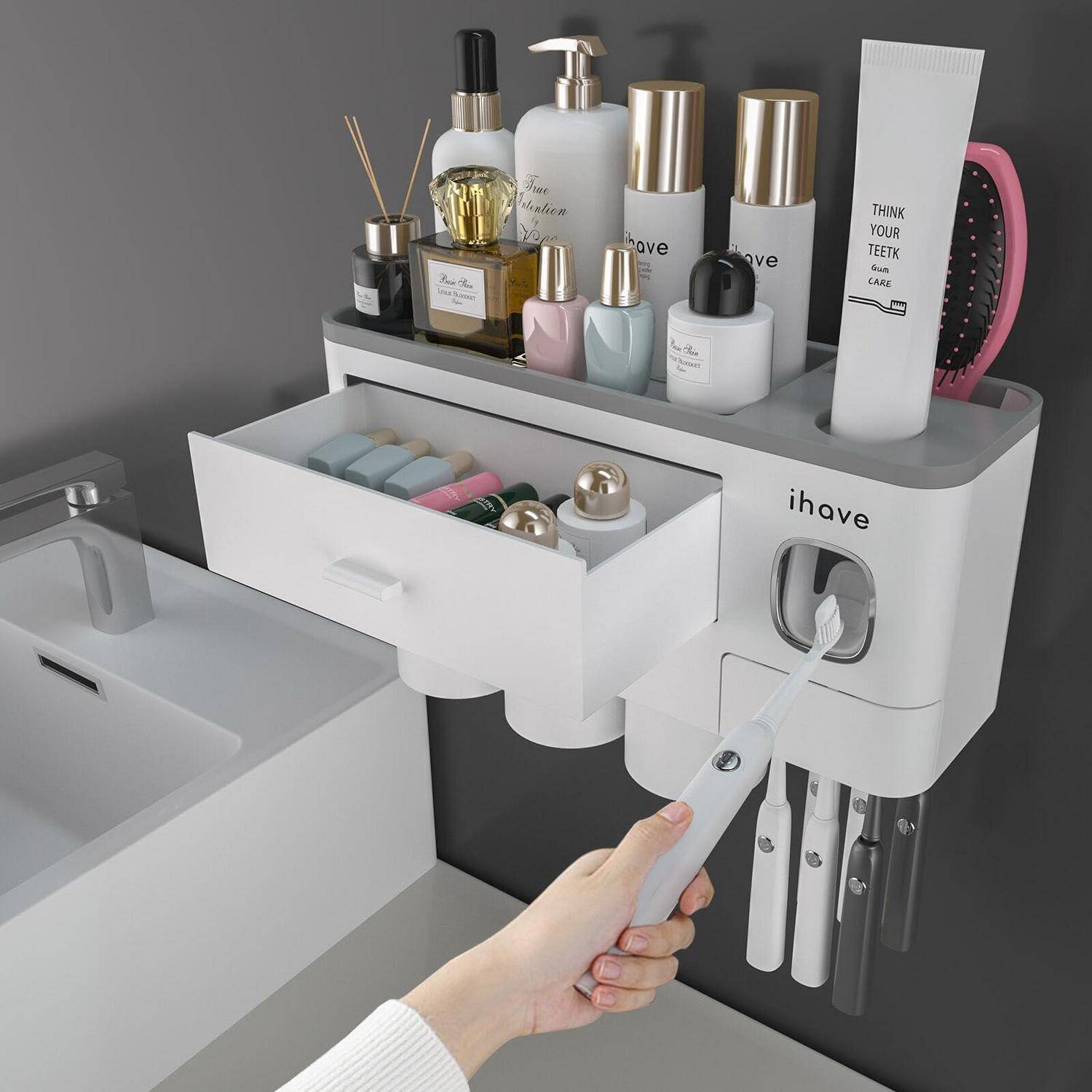 Hand hält eine elektrische Zahnbürste in der Nähe eines Badezimmerorganizers mit Zahnpasta, Hautpflegeflaschen und Zahnbürsten neben einem Waschbecken.
