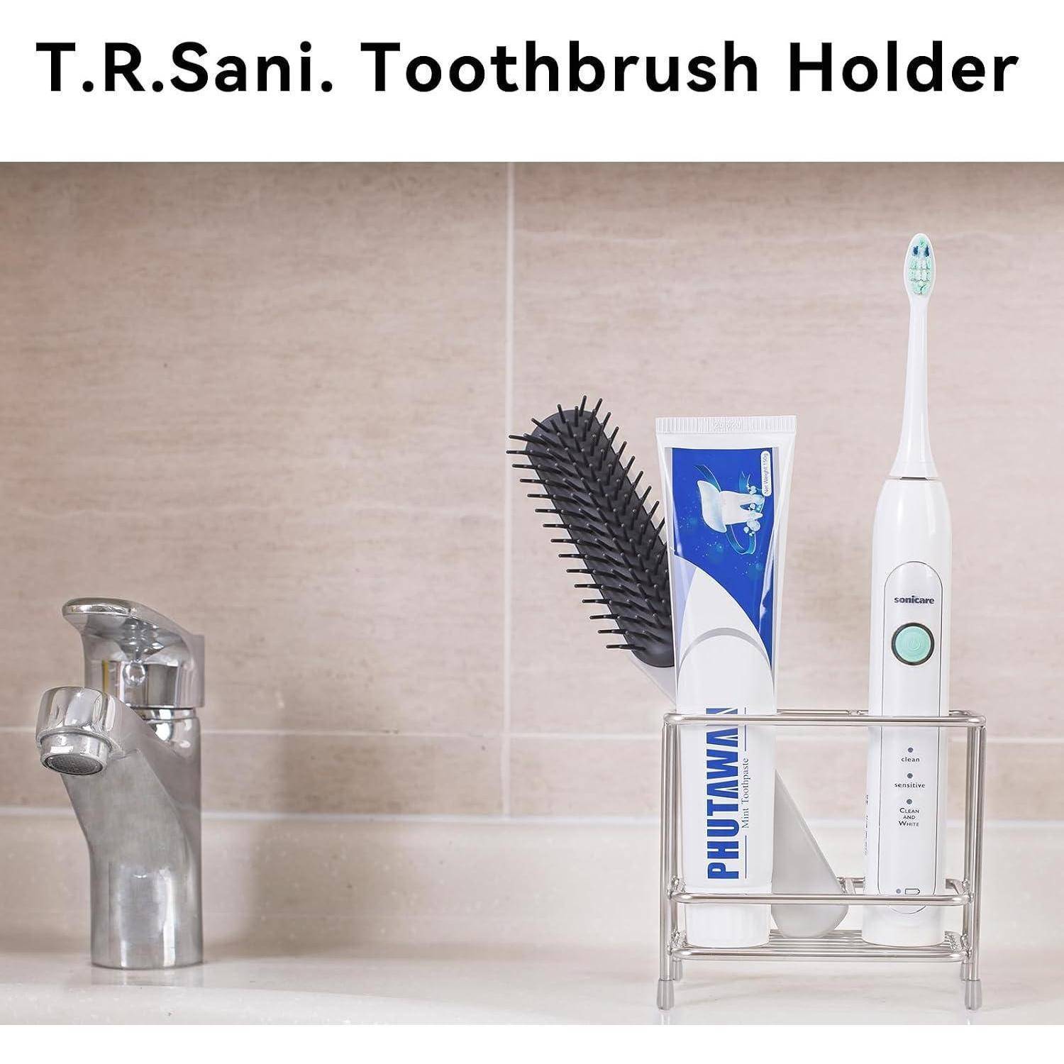 Badezimmer-Arbeitsplatte mit einem durchsichtigen Zahnbürstenhalter, der eine elektrische Zahnbürste, Zahnpasta und einen Kamm neben einem Wasserhahn hält; beschriftet mit „T.R.Sani. Zahnbürstenhalter