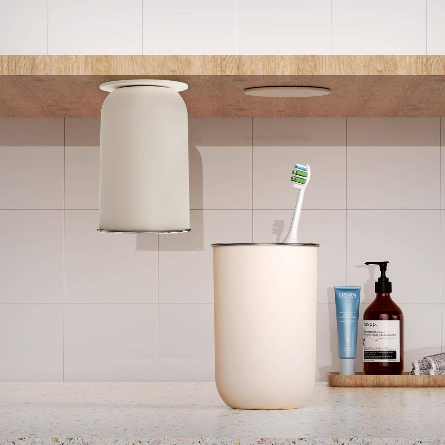 Minimalistische Badezimmerablage mit einer cremefarbenen Zahnbürste in einem Becher, Lotion- und Seifenspendern sowie einem wandmontierten Mülleimer darüber.