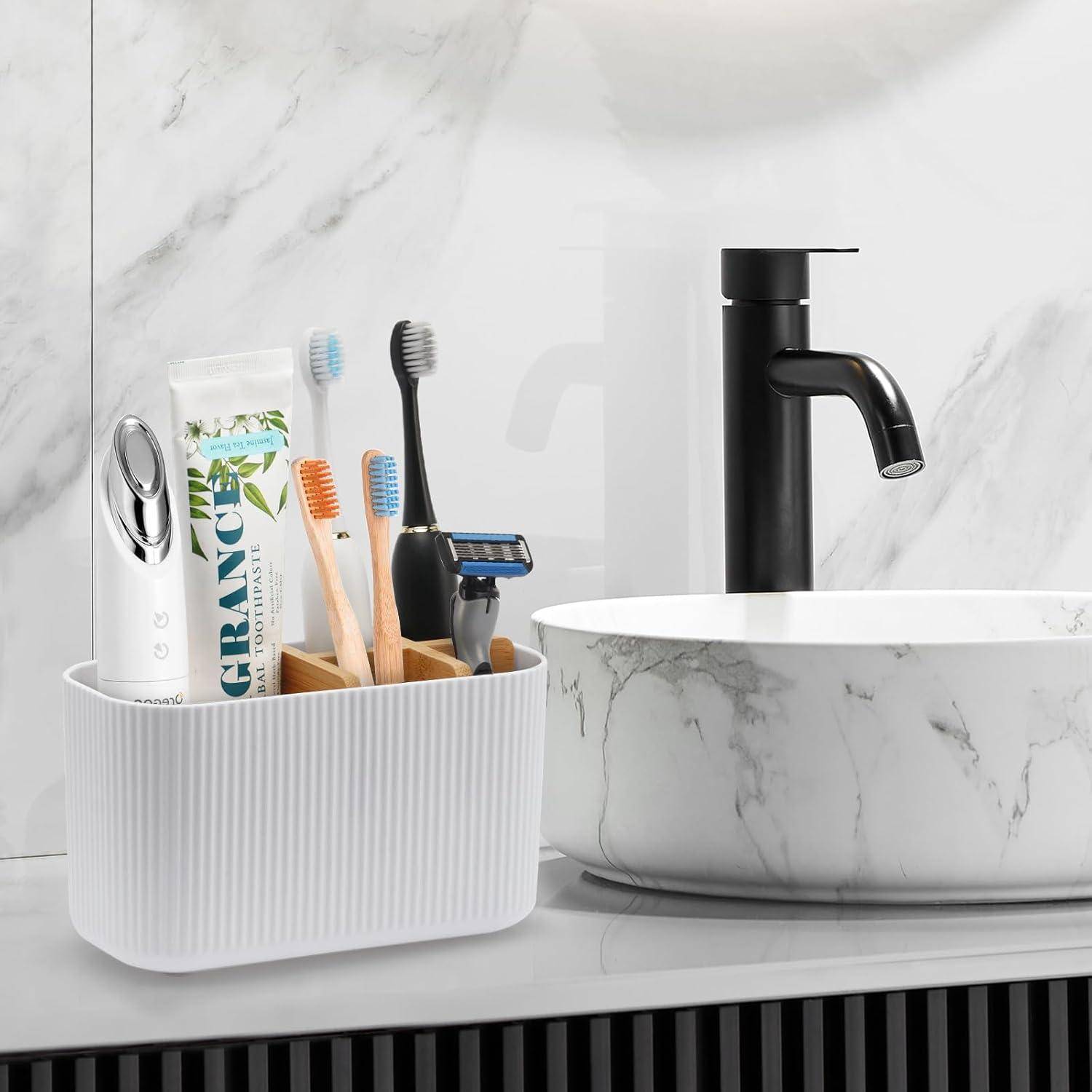 Badezimmerablagefläche mit einem Zahnbürstenorganizer, einer elektrischen Zahnbürste, Zahnpasta, manuellen Zahnbürsten und einem Rasierer neben einem Marmorbecken mit schwarzem Wasserhahn.