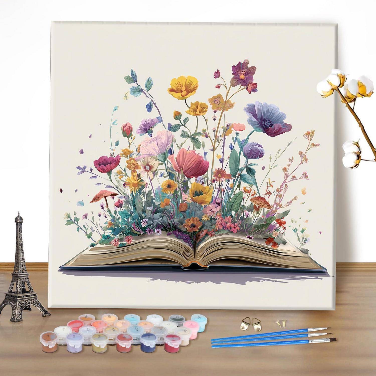 Gemaltes aufgeschlagenes Buch mit bunten Blumen, die aus seinen Seiten hervorbrechen, auf einem Schreibtisch neben Farbtöpfen, Pinseln und einem kleinen Eiffelturm-Modell angezeigt.