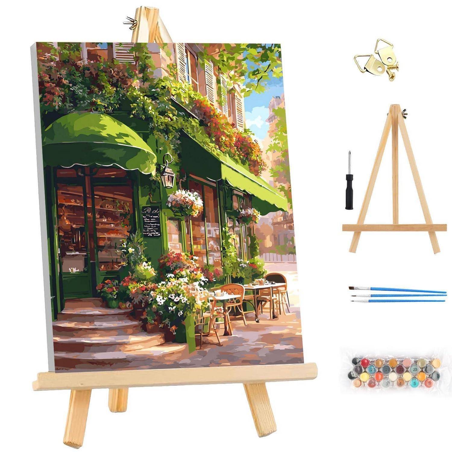 Staffelei zeigt ein Gemälde einer blumengeschmückten Café-Fassade mit grüner Markise, dargestellt mit der Staffelei und Malwerkzeugen auf weißem Hintergrund.