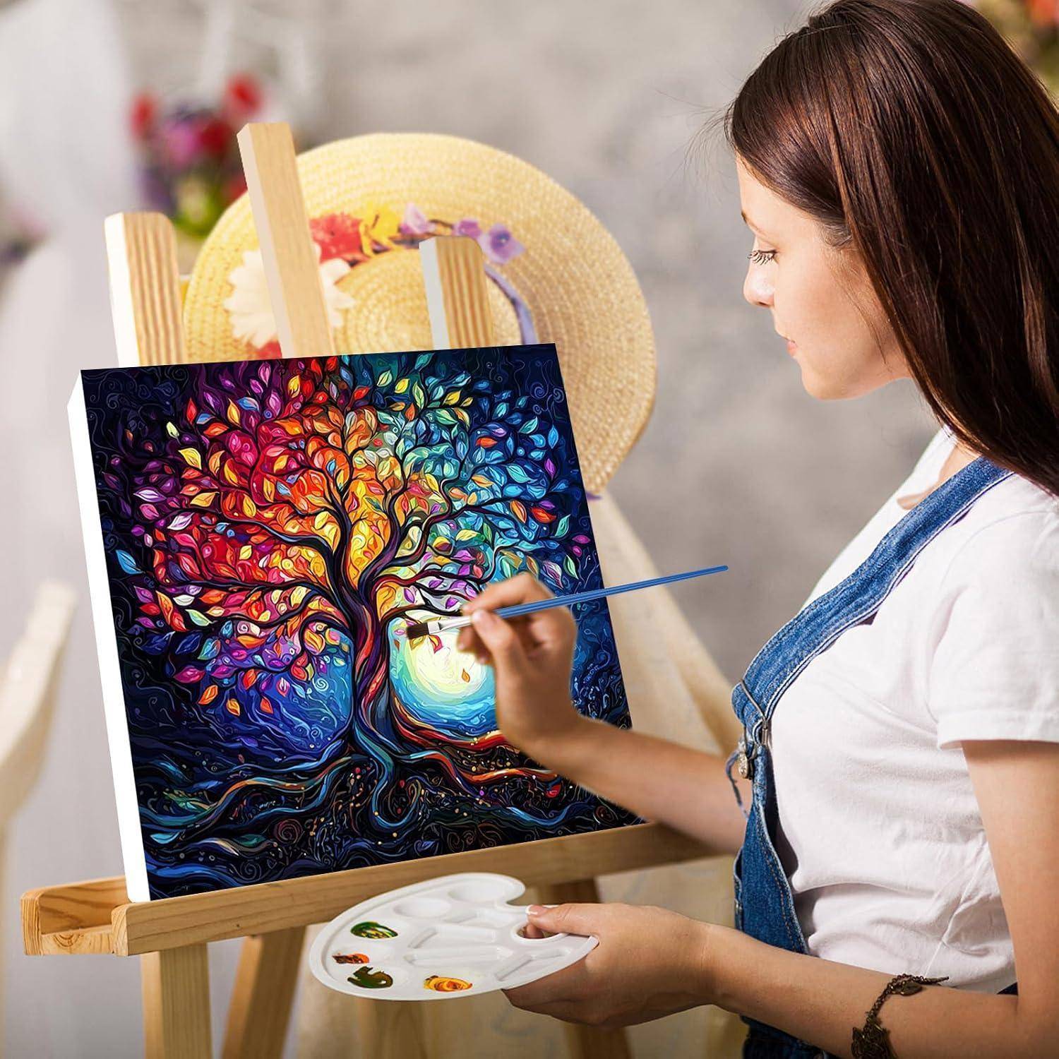 Eine Frau, die einen farbenfrohen Baum auf einer Staffelei malt, hält eine Palette in einem Kunstatelier.