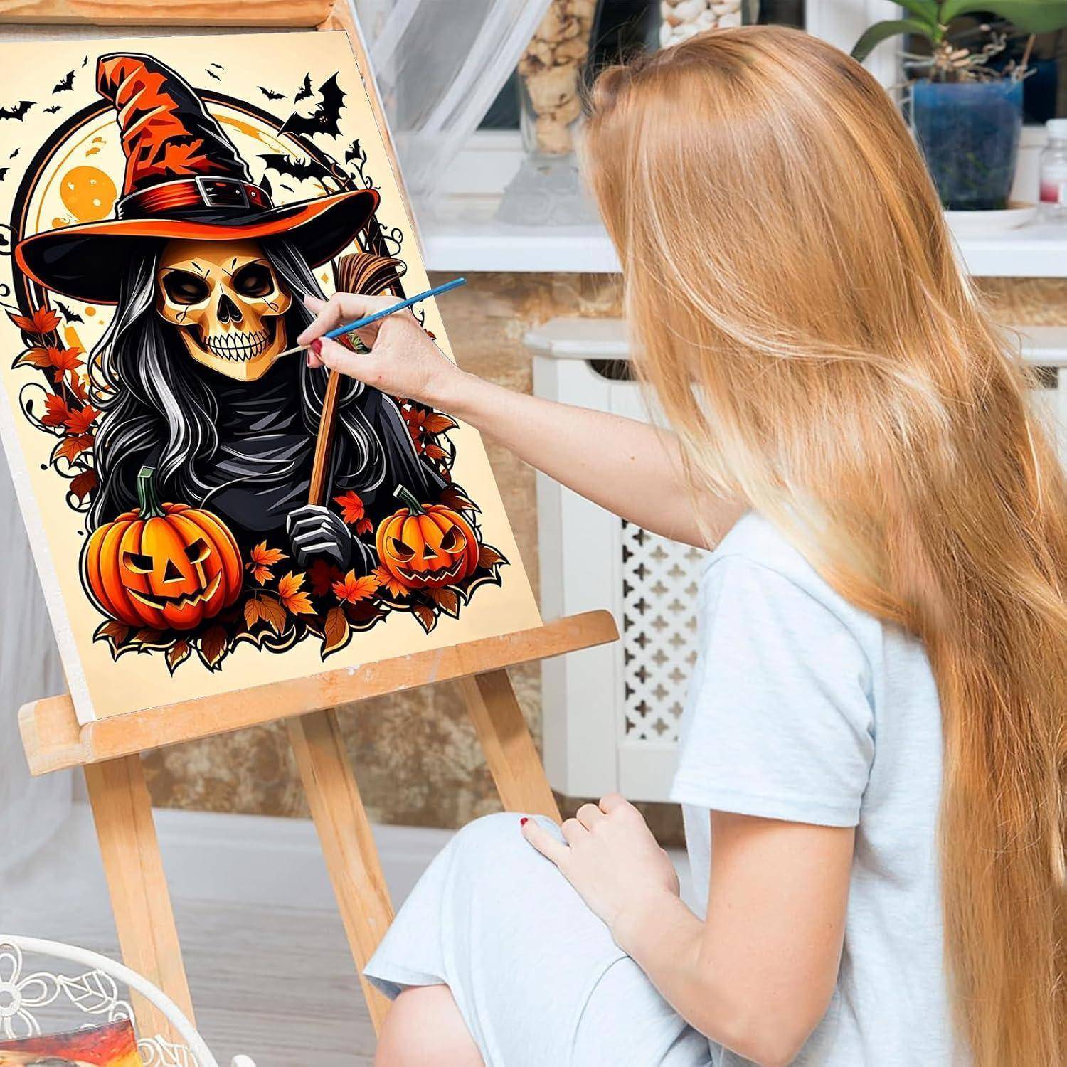 Frau, die eine Halloween-Illustration eines Schädels in einem Hexenhut mit Kürbissen auf einer Staffelei malt.