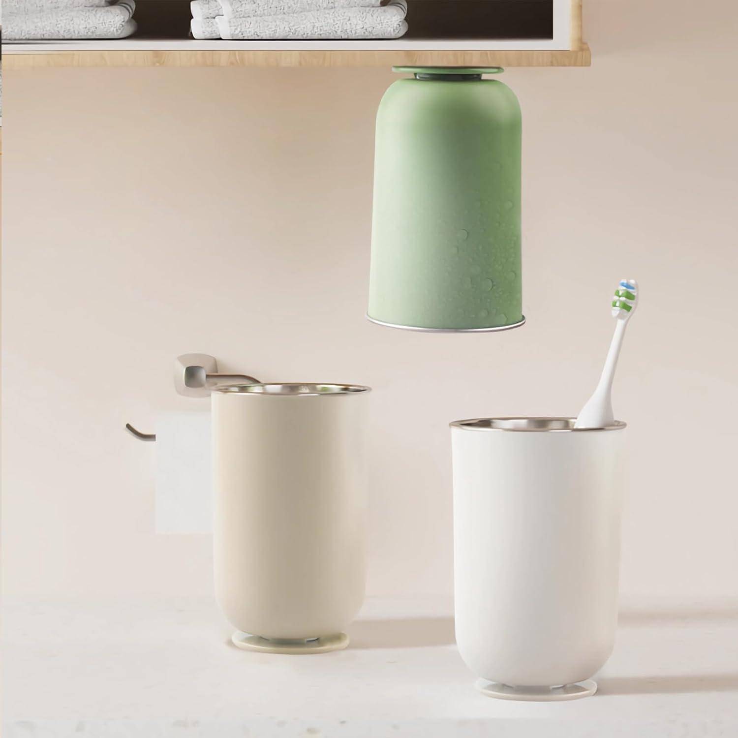 Drei minimalistische Badezimmergläser in Creme, Weiß und Mintgrün stehen auf einer hellen Arbeitsplatte, eines davon mit einer Zahnbürste.