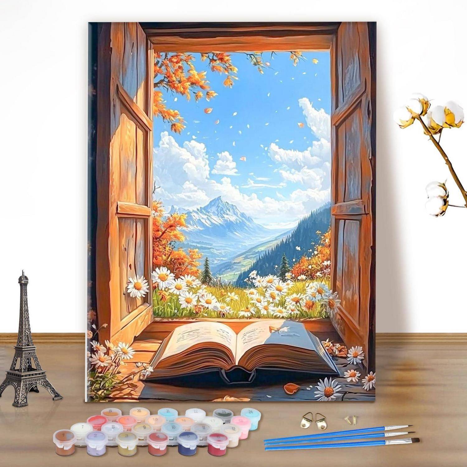 Ein aufgeschlagenes Buch auf einer Staffelei zeigt eine sonnige Berglandschaft, die von hölzernen Fensterläden eingerahmt wird, mit Kunstmaterialien darunter angeordnet.