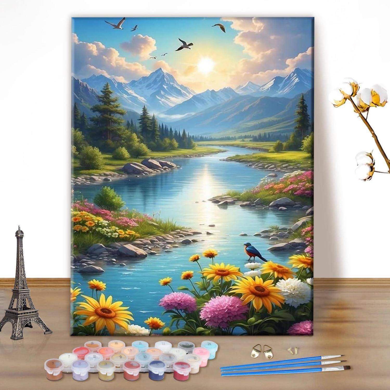 Ein farbenfrohes Landschaftsgemälde eines Bergflusses mit Blumen, Vögeln und Sonnenlicht, ausgestellt mit Malutensilien auf einem Tisch.