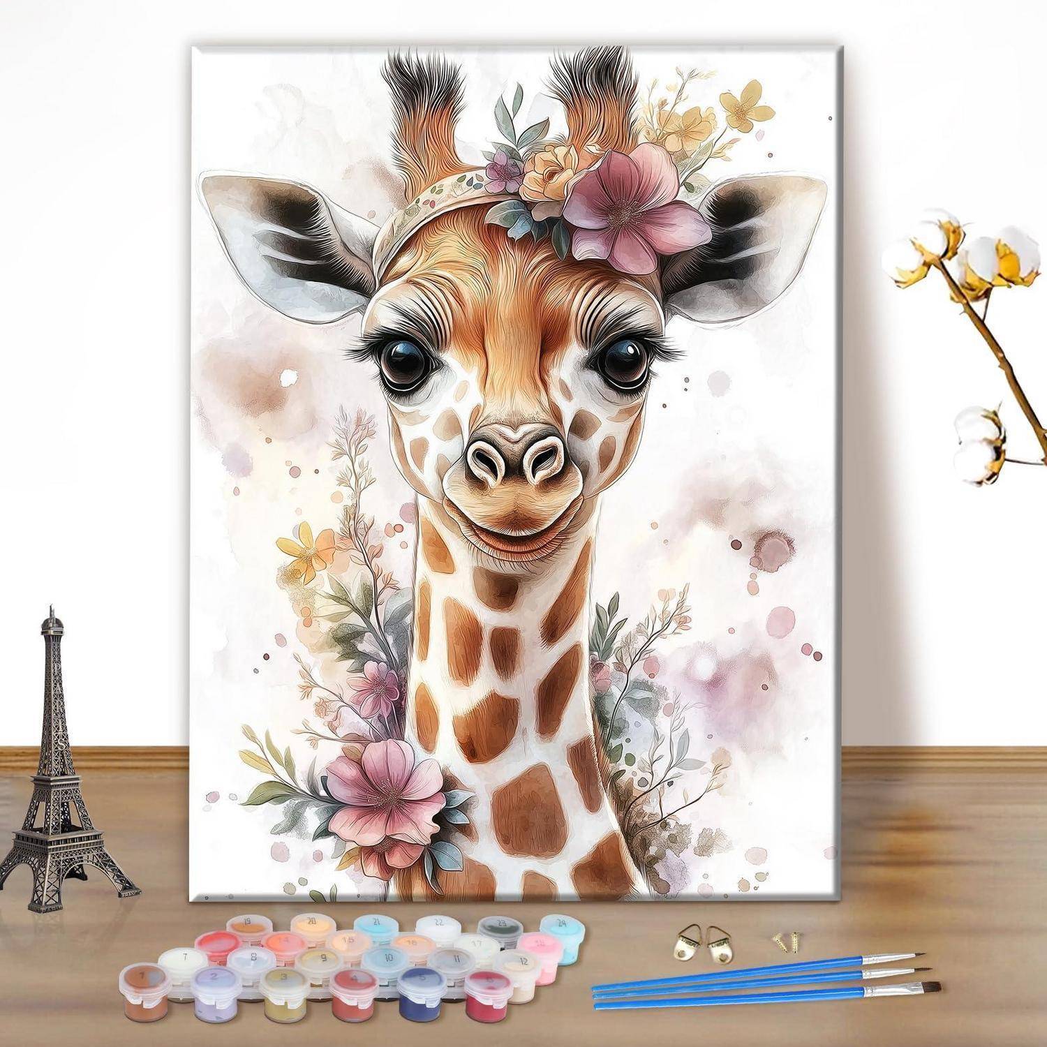 Malen-nach-Zahlen-Set mit einem Aquarell-Giraffenporträt mit Blumen, dargestellt auf einer Leinwand mit Farbdosen, Pinseln und einem Miniatur-Eiffelturm auf einem Tisch.
