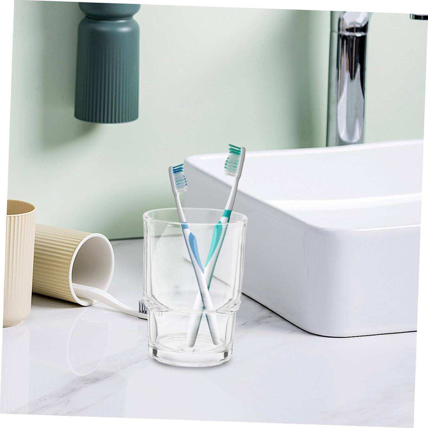 Zwei Zahnbürsten in einem klaren Glas neben einem Badezimmerbecken, mit einer umgestürzten Tasse in der Nähe.