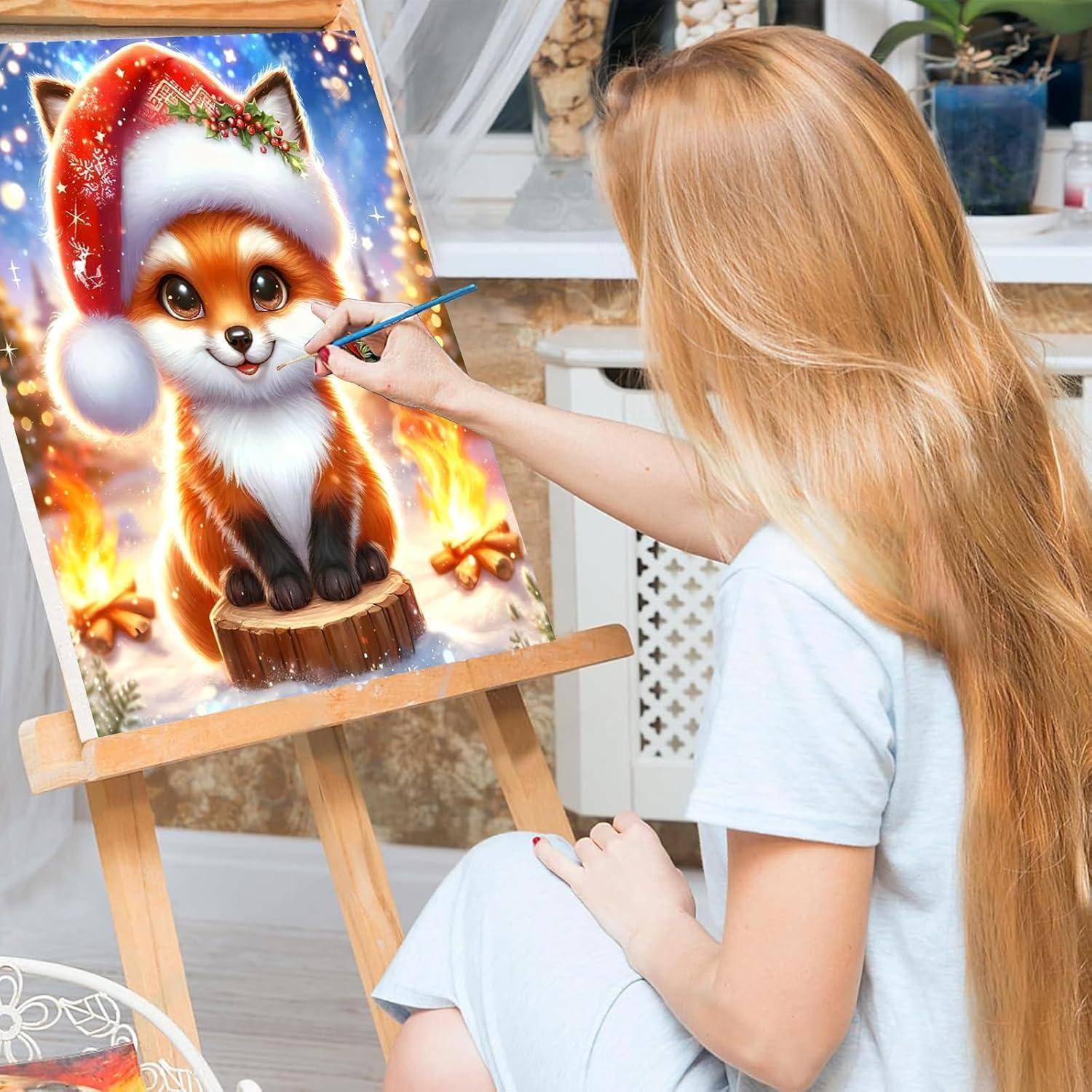 Junge Frau malt einen festlichen Cartoon-Fuchs mit Weihnachtsmütze auf einer Staffelei im Innenraum.