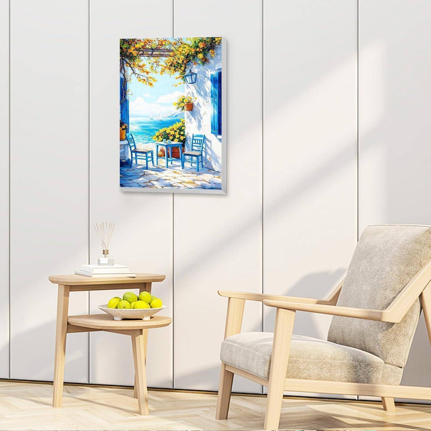 Gerahmtes Gemälde einer Strandterrasse über einem kleinen Beistelltisch mit einer Obstschale daneben und einem beigen Sessel in einem hellen Raum.