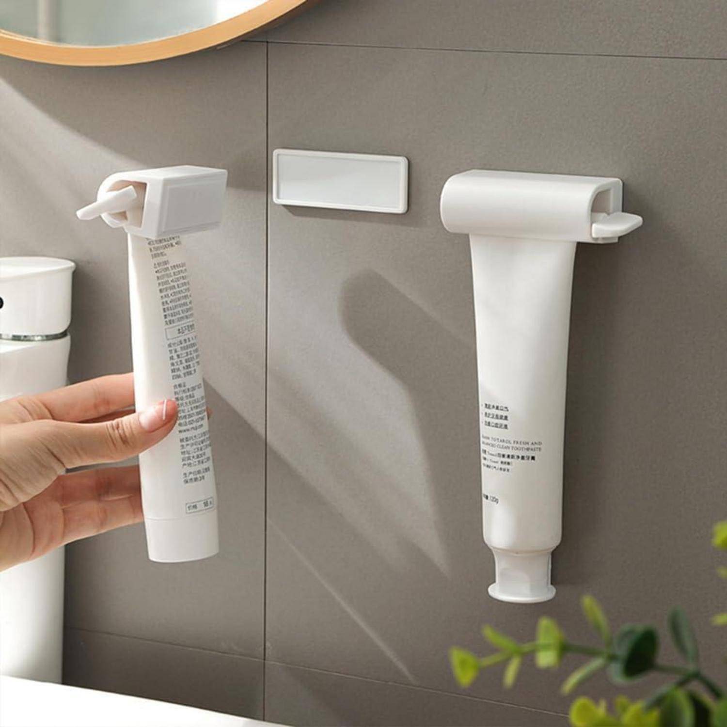 Zwei wandmontierte Zahnpastatuben mit Spendern im Badezimmer; eine wird von einer Hand hochgehalten.