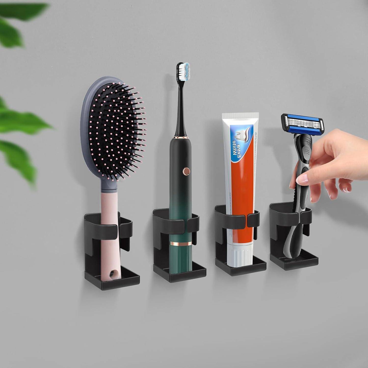 Wandmontierte schwarze Halter organisieren an einer grauen Wand eine Haarbürste, eine elektrische Zahnbürste, Zahnpasta und einen Rasierer; eine Hand platziert den Rasierer.
