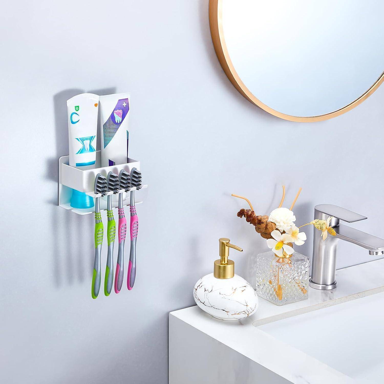 Badezimmerwaschbeckenbereich mit einem wandmontierten Zahnbürstenhalter, der vier Zahnbürsten und Zahnpasta hält, neben einem Seifenspender, Blumen und einem Wasserhahn.