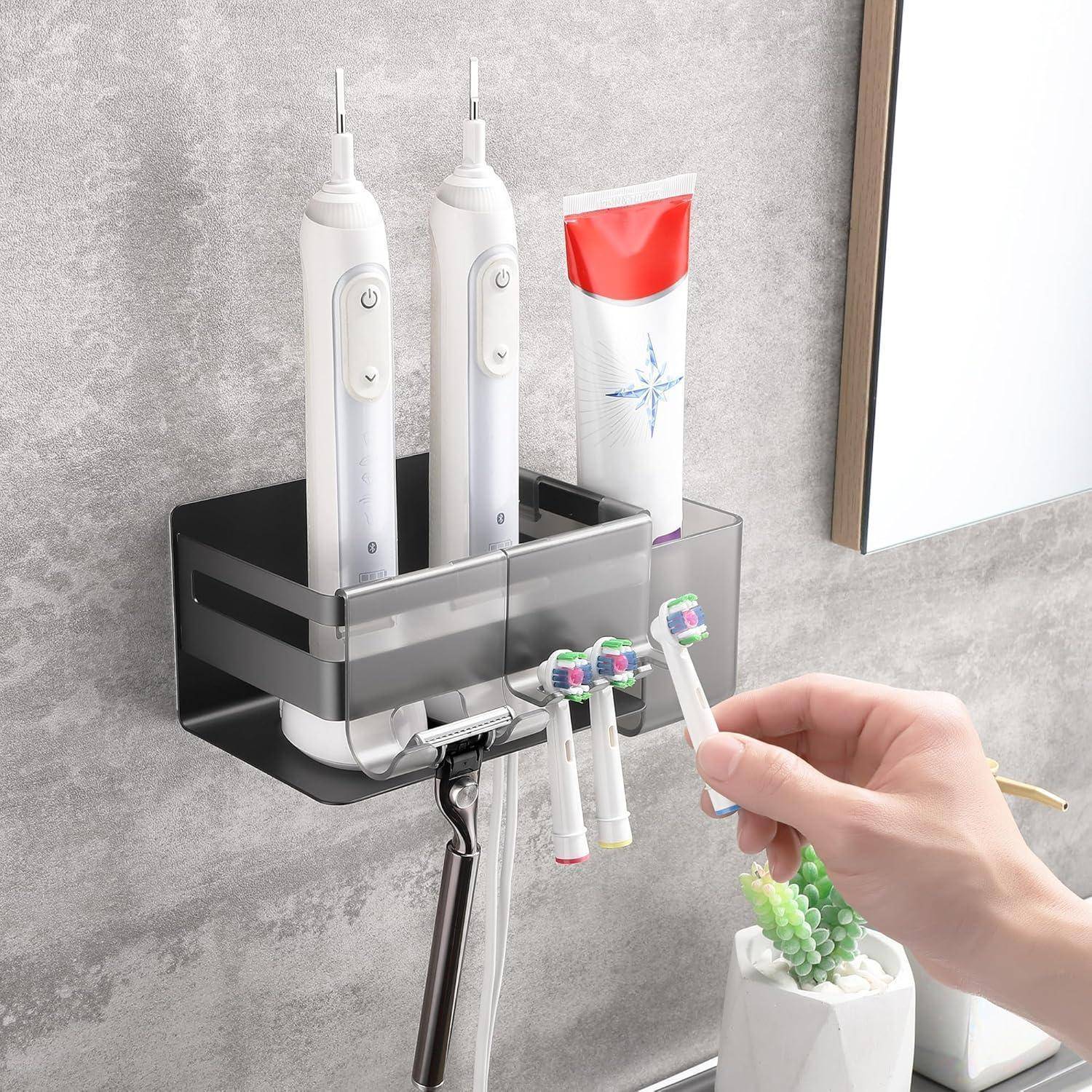 Wandmontierter Badezimmerorganizer mit zwei elektrischen Zahnbürsten, Zahnpasta und Ersatzbürstenköpfen; eine Hand nimmt einen Bürstenkopf auf.