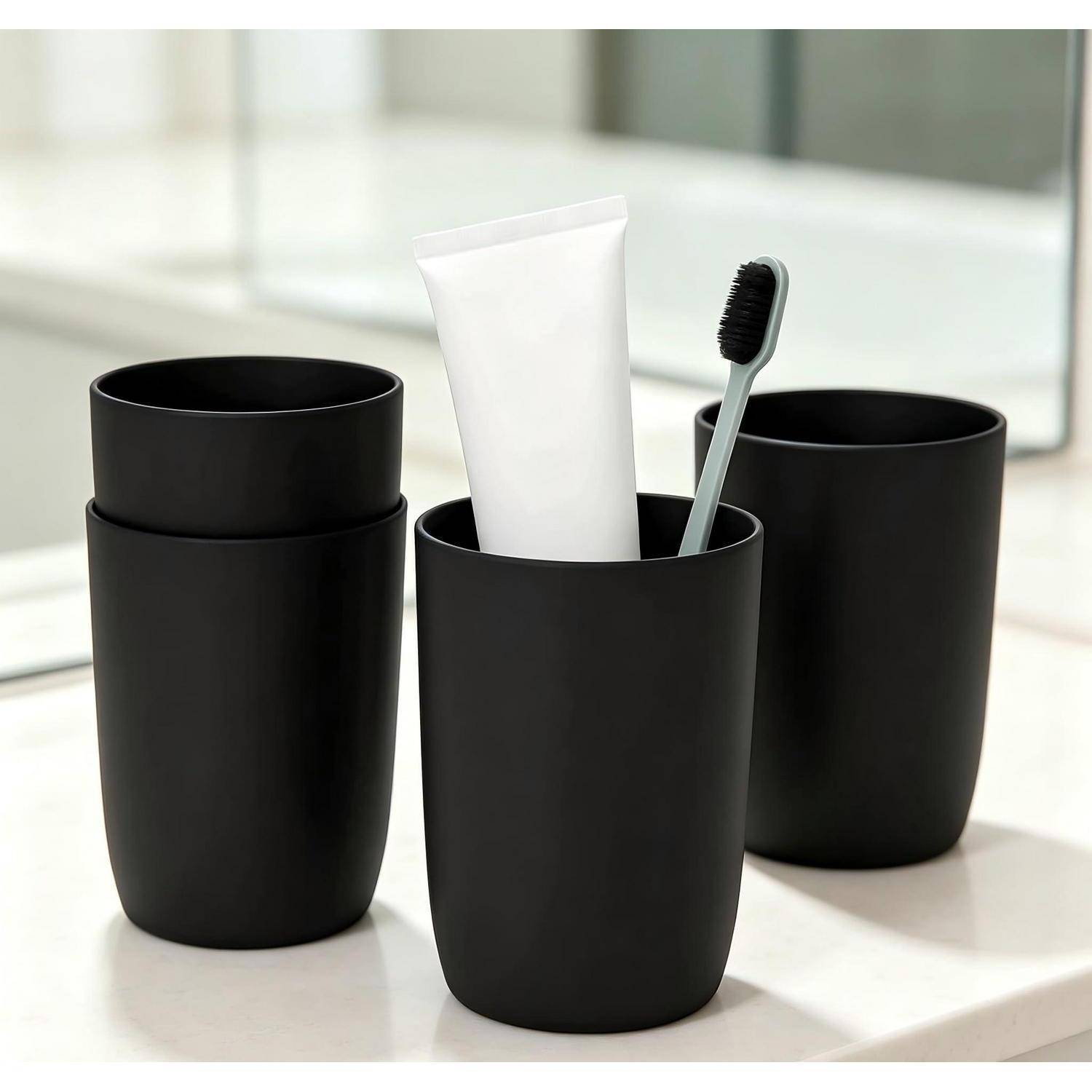 Drei matte schwarze Badezimmertassen auf einer weißen Arbeitsplatte, wobei die mittlere Tasse eine weiße Zahnpastatube und eine Zahnbürste enthält.