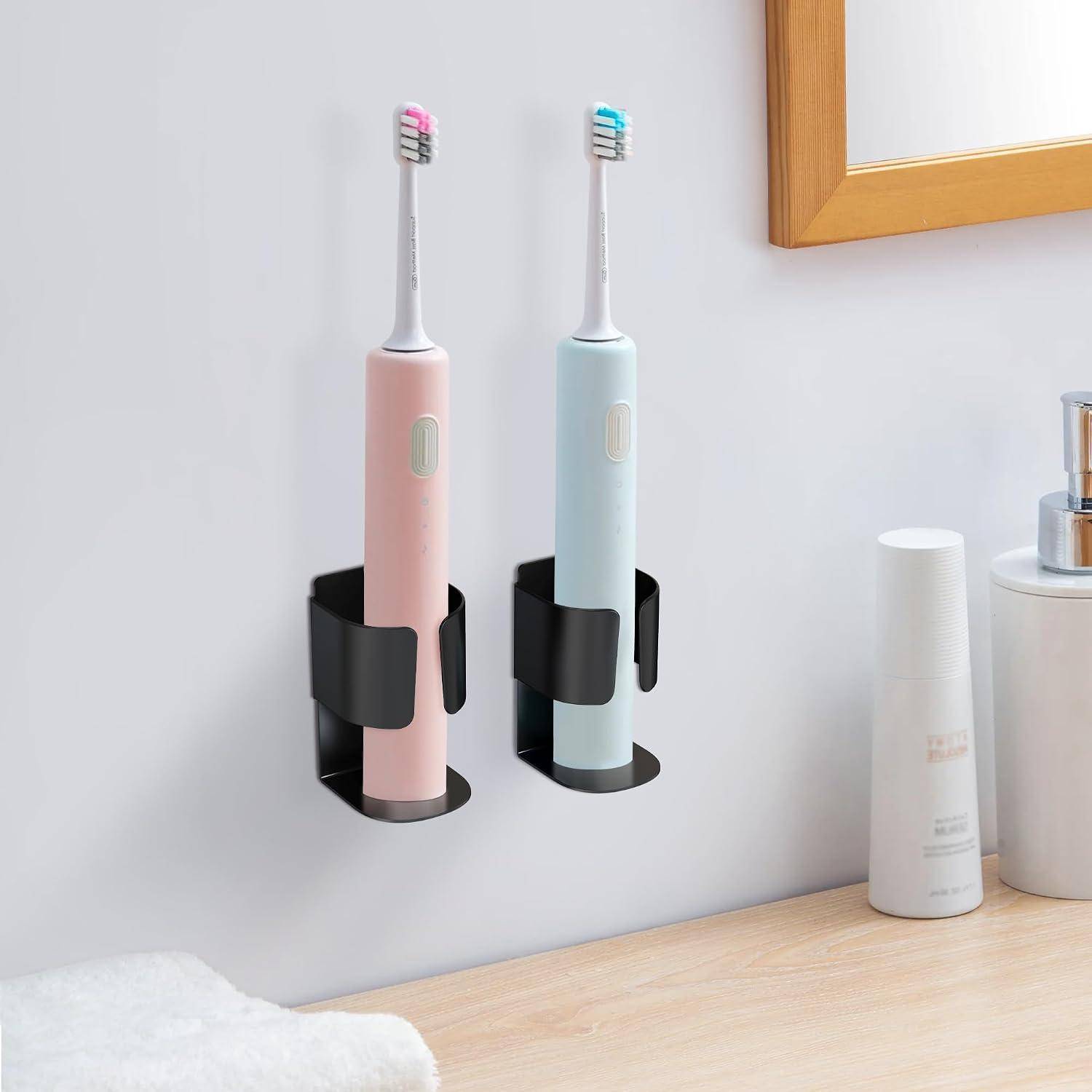 Zwei elektrische Zahnbürsten, eine rosa und eine hellblau, stehen in wandmontierten Haltern über einem Badezimmerschrank.