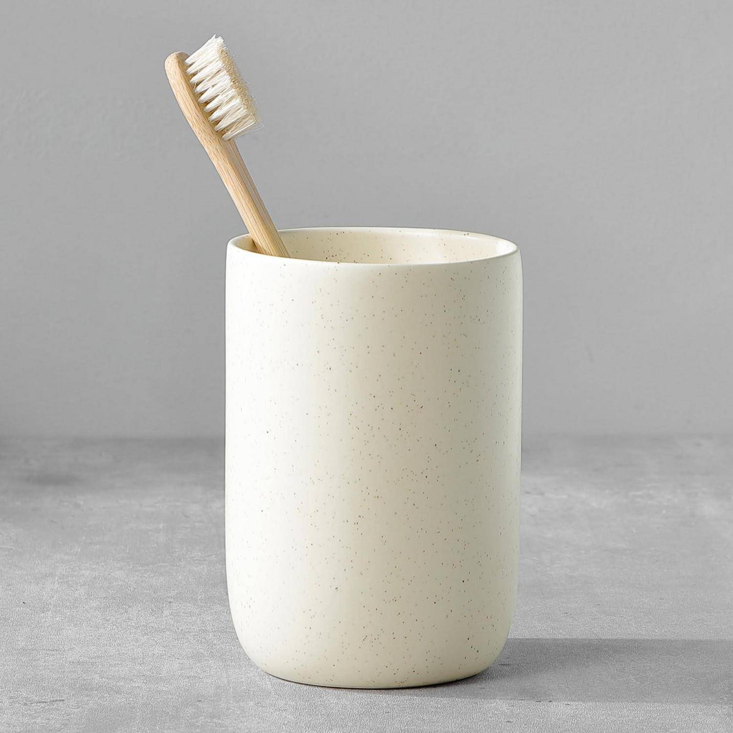 Bambuszahnbürste, die in einer weißen Keramiktasse auf einer grauen Oberfläche steht.