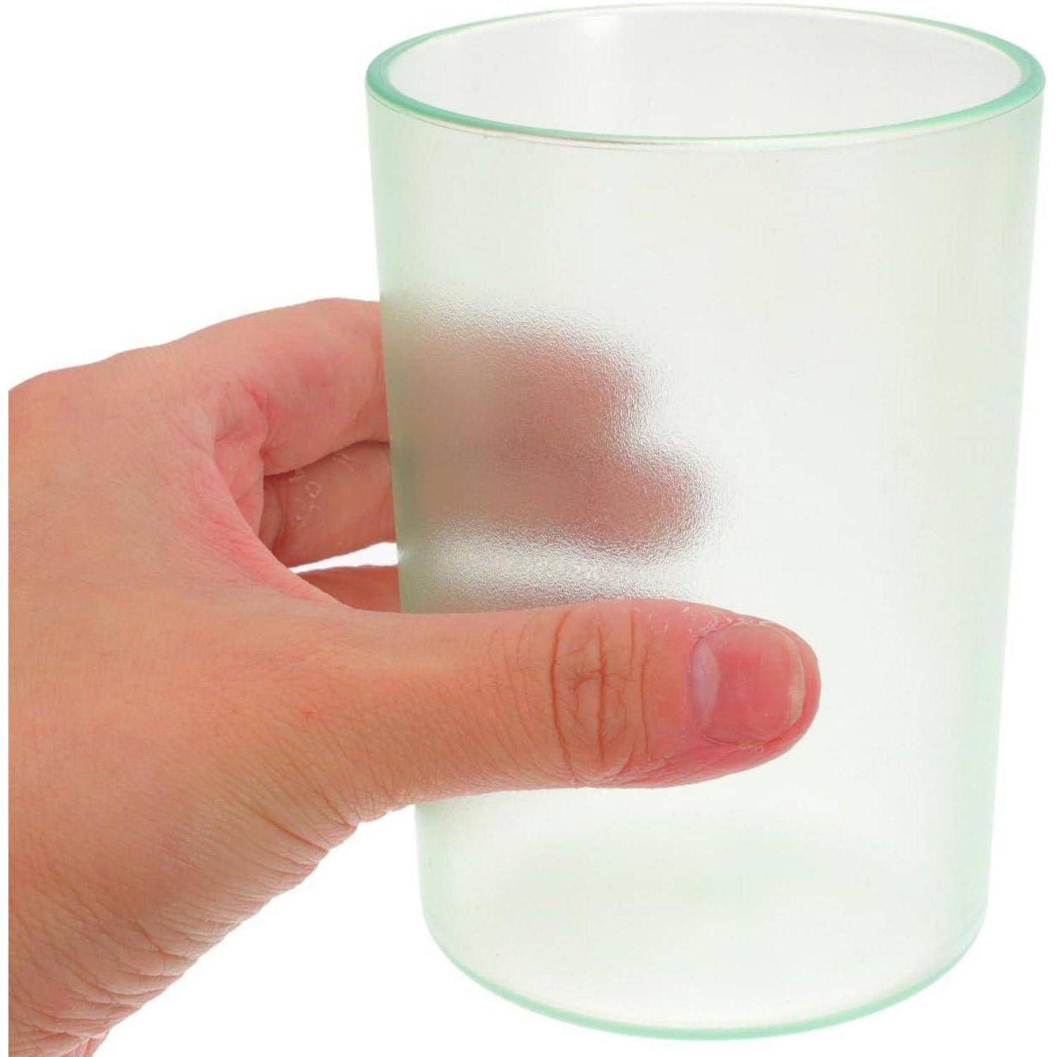 Eine Hand, die ein mattiertes durchsichtiges Glastumbler auf weißem Hintergrund hält.