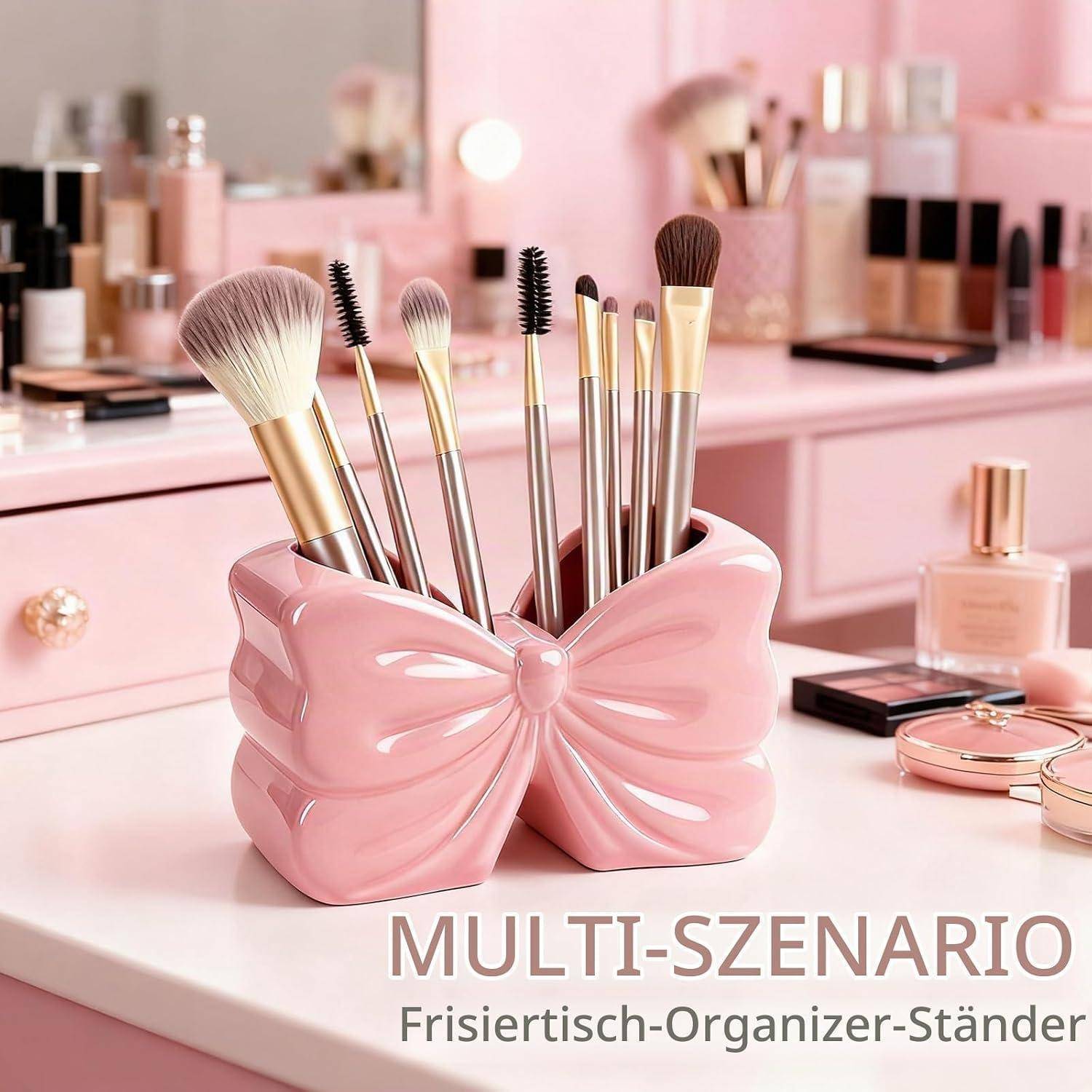 Rosa schleifenförmiger Makeup-Pinselhalter auf einem Frisiertisch, der mehrere Kosmetikpinsel hält; Makeup-Flaschen und Paletten befinden sich im Hintergrund.