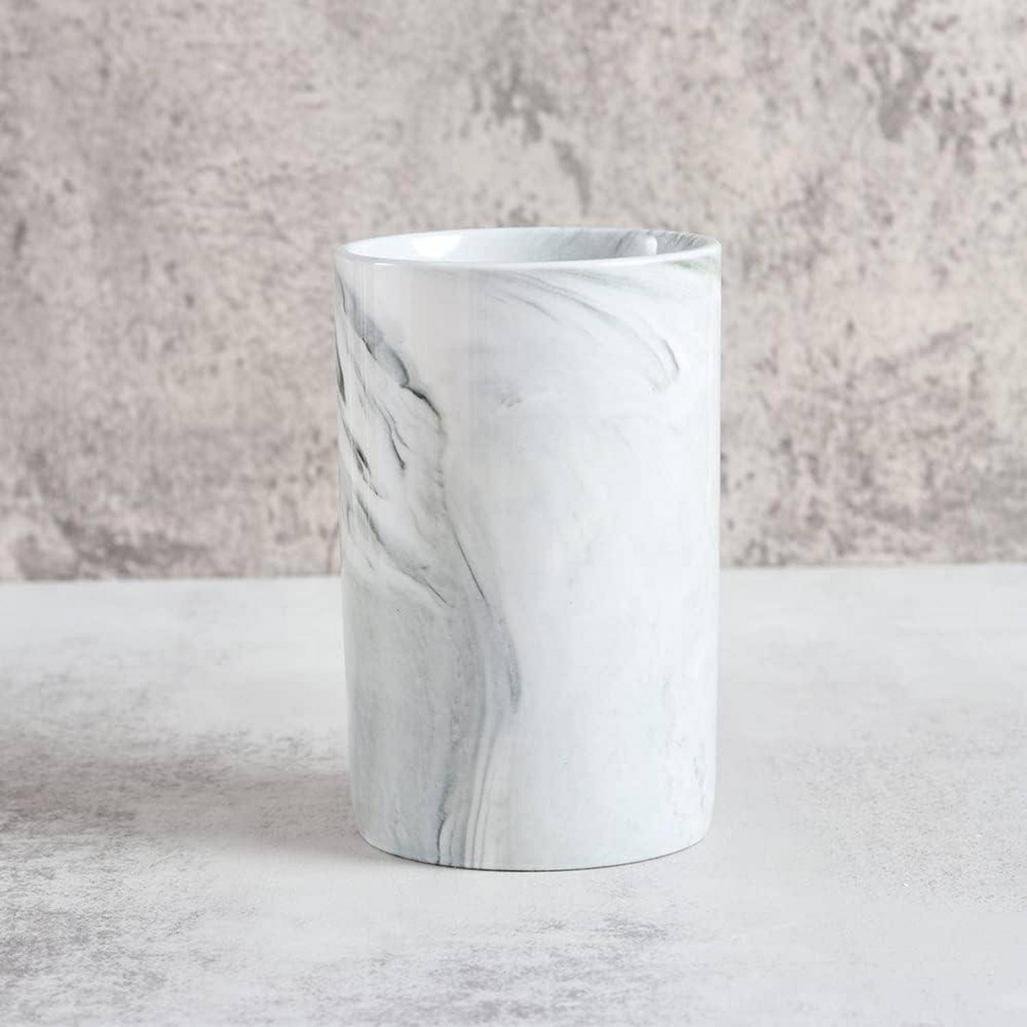 Weiße Vase oder Tasse mit Marmormuster in Zylinderform auf einer hellgrauen Oberfläche vor einem strukturierten grauen Hintergrund.