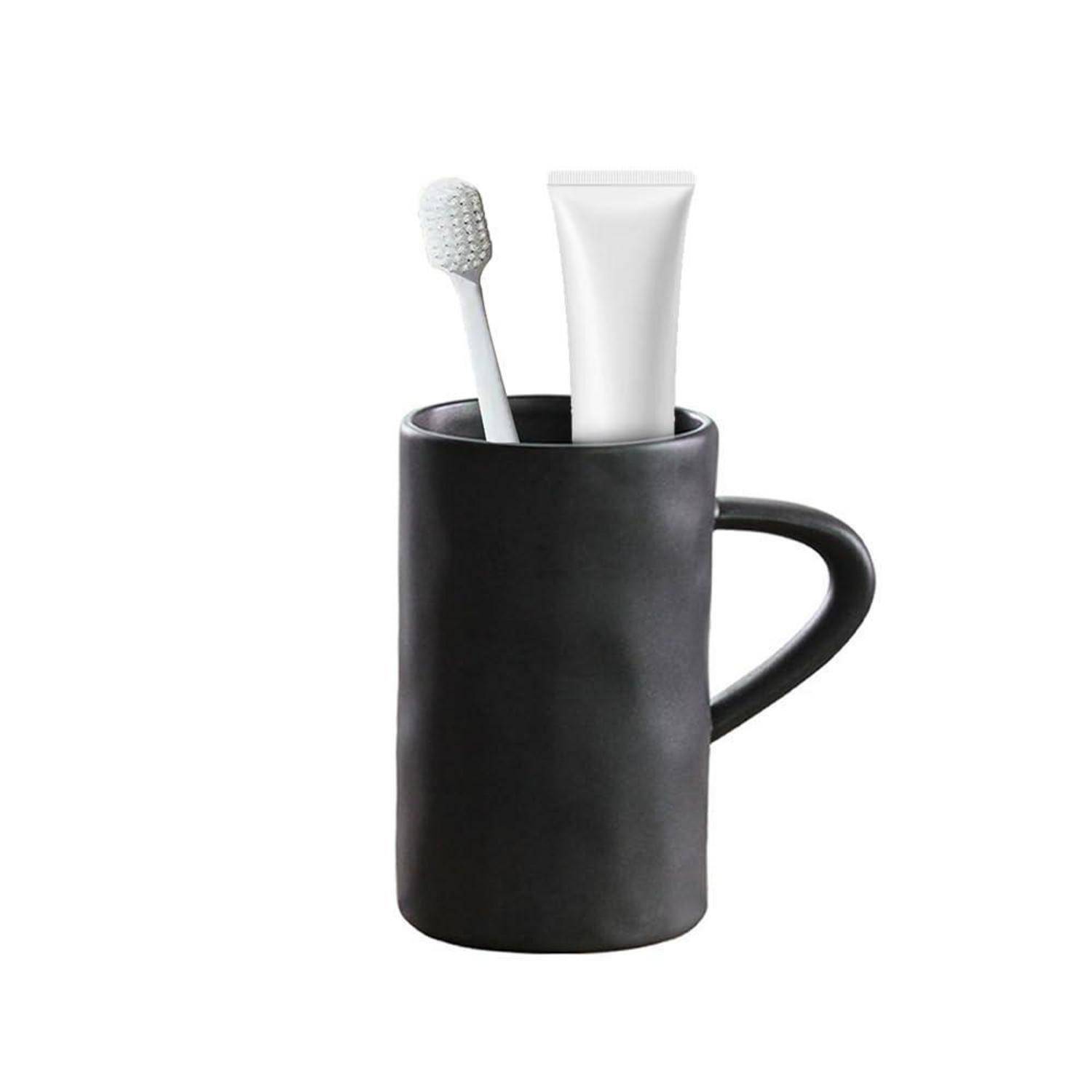 Schwarze Tasse, die eine Zahnbürste und eine Zahnpastatube hält, was auf ein Badezimmer- oder Reise-Zahnpflegeset hindeutet.