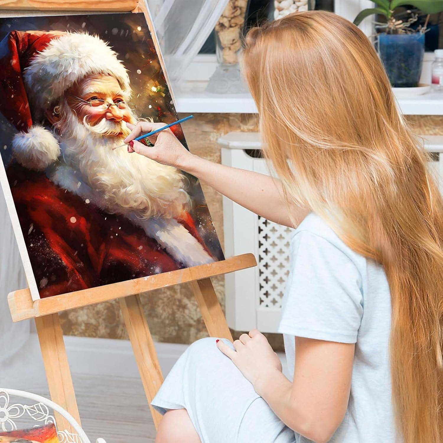 Eine junge Frau malt ein Porträt des Weihnachtsmanns auf einer Staffelei in einem hellen Raum.