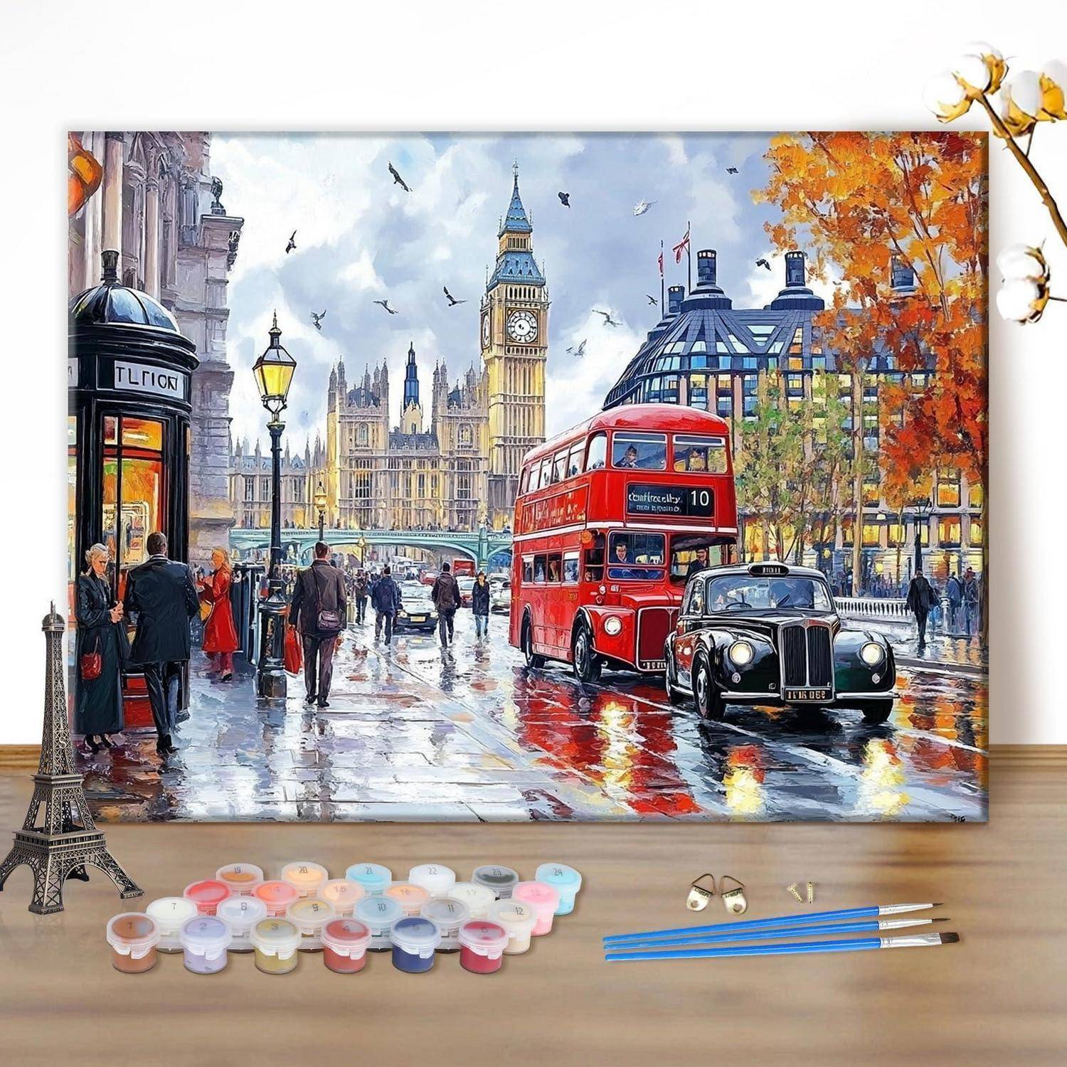 Gemälde eines regnerischen London mit Big Ben, einem roten Doppeldeckerbus, einem schwarzen Taxi, Fußgängern und Herbstbäumen auf einer Staffelei ausgestellt, mit Farbdosen und Pinseln darunter.